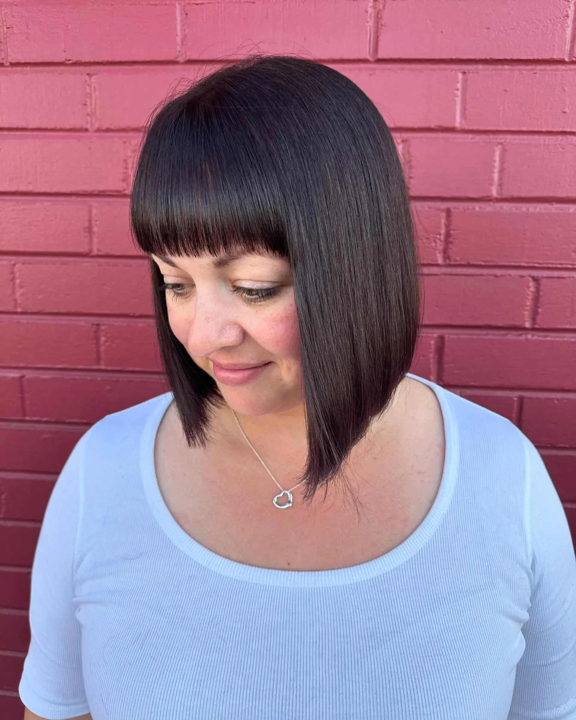 A sleek chin-length blunt bob featuring full straight-across bangs in a deep espresso brunette tone. 1