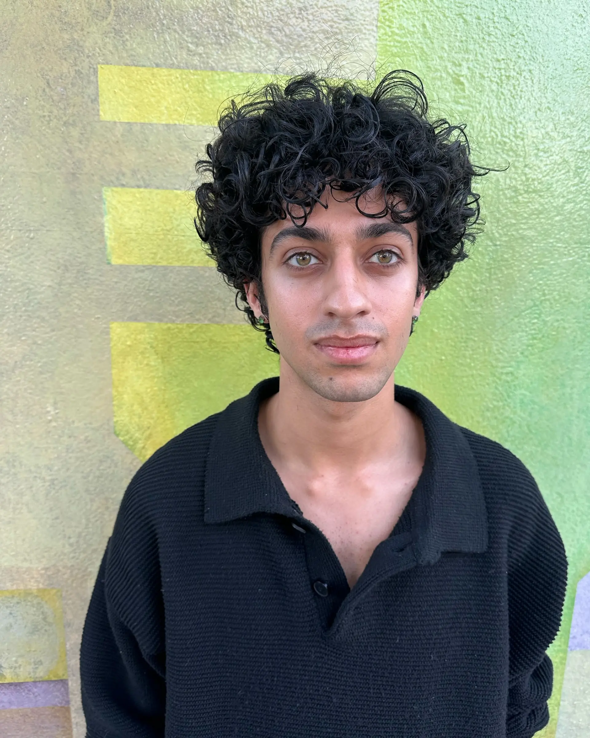 A defined short curly haircut with volume on top and soft curly bangs framing the forehead. 1