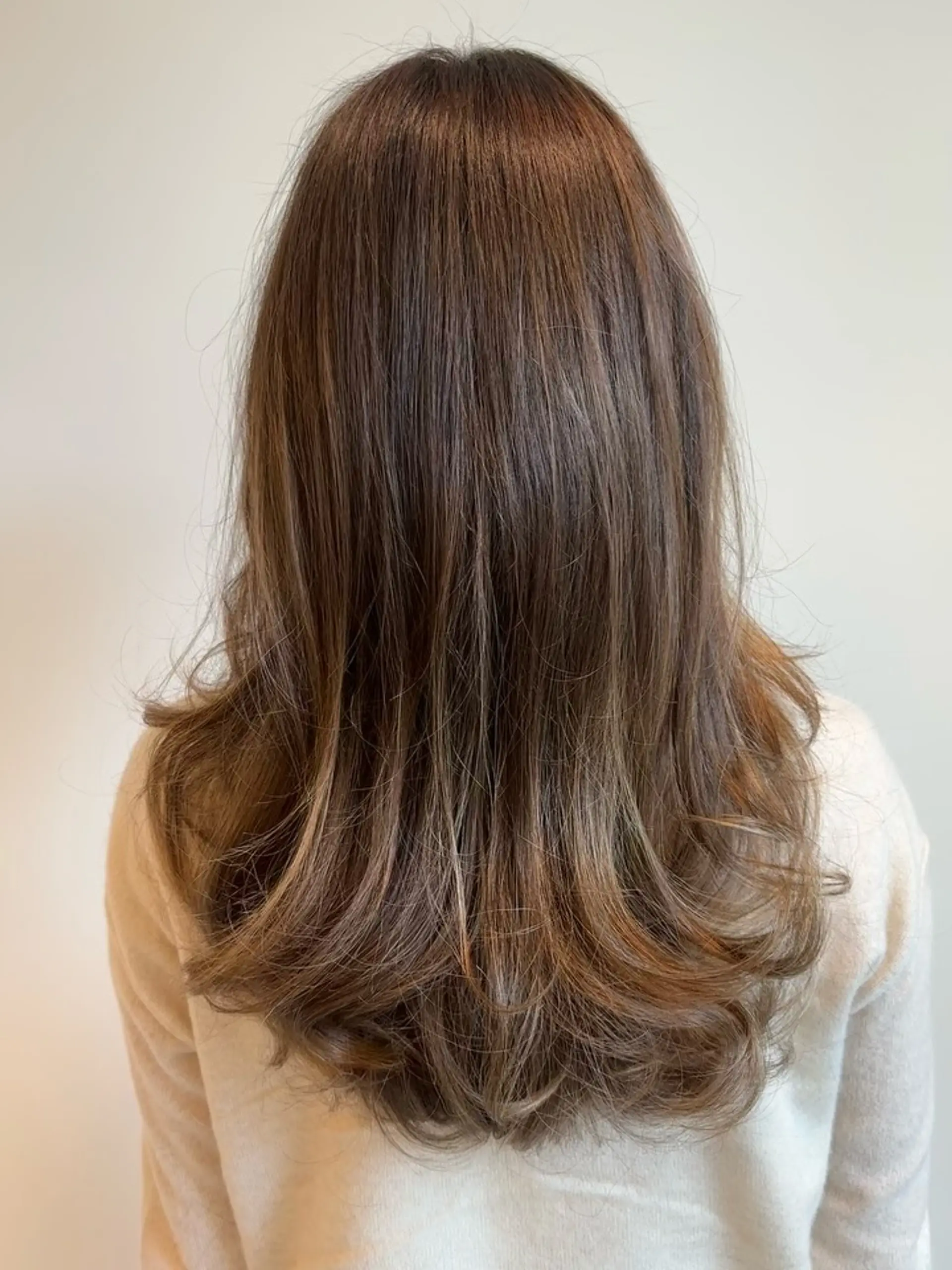 Long brunette hair featuring a seamless golden balayage with voluminous, inward-curled ends. 1