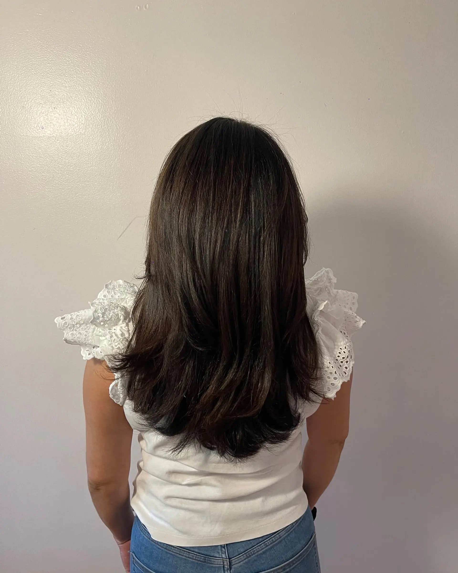 Long dark brunette hair cut with seamless, cascading layers and styled into a voluminous, smooth blowout. 1