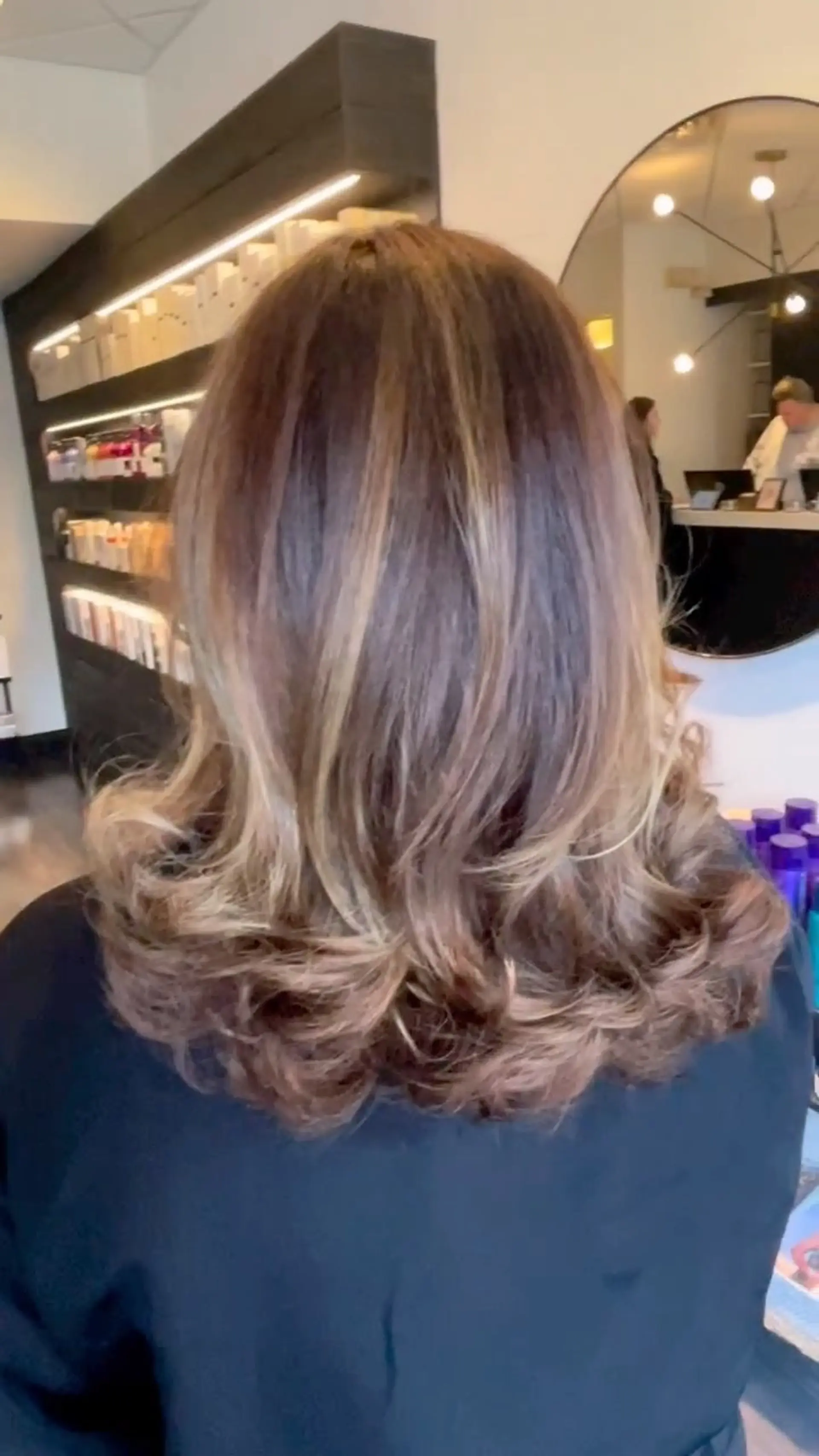 Medium-length dimensional brunette hair with soft caramel balayage, styled with full, bouncy curls at the ends. 1