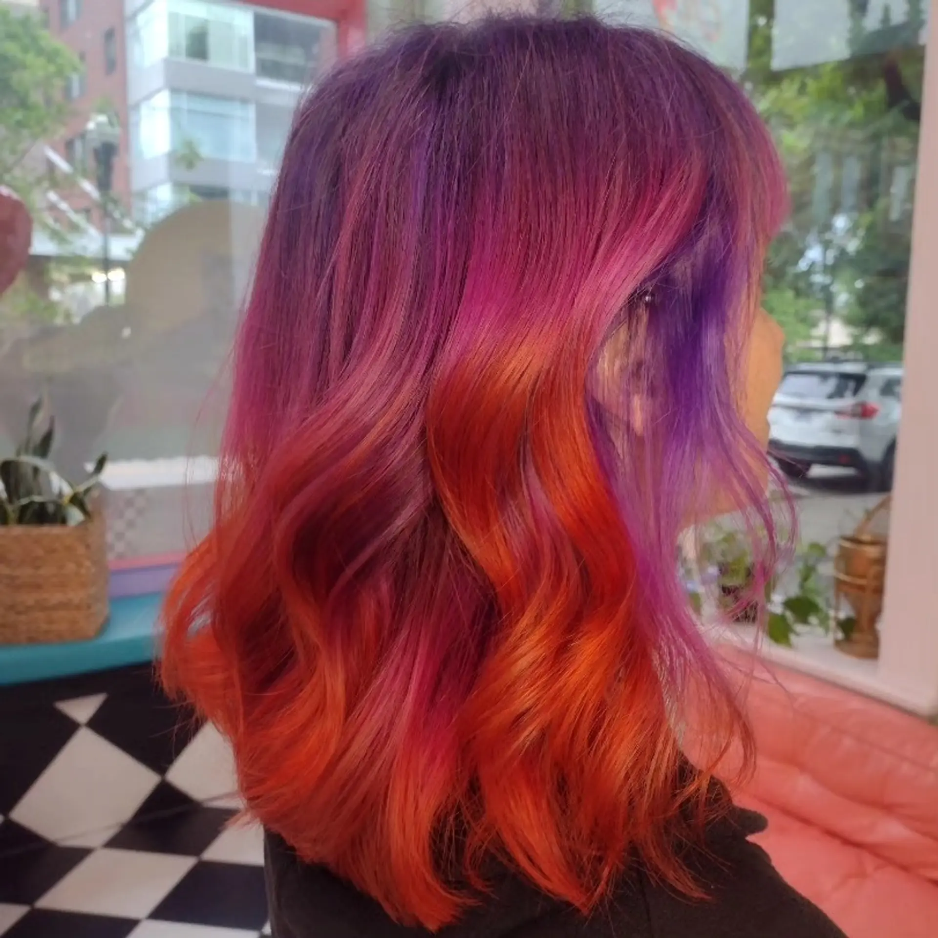 Vibrant sunset-inspired vivid color melt transitioning from deep purple roots to hot pink mid-lengths and bright orange ends, styled with loose waves. 1