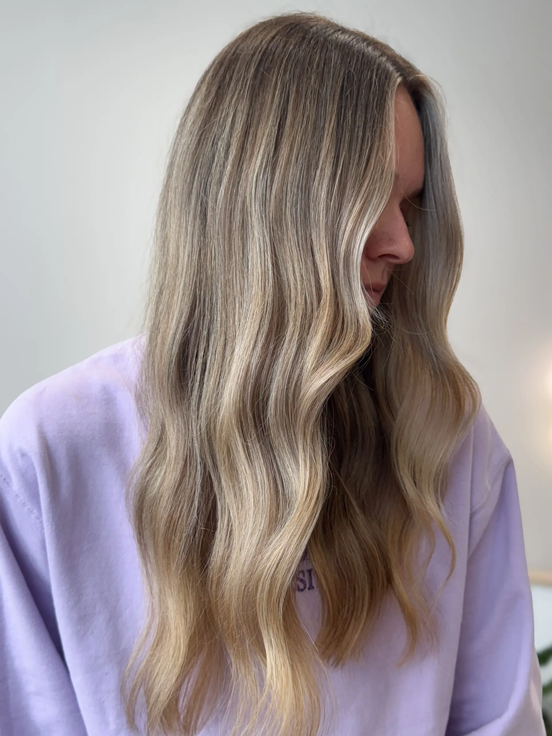 Long hair styled in soft, loose waves featuring a seamless blend of dimensional soft blonde tones. 1
