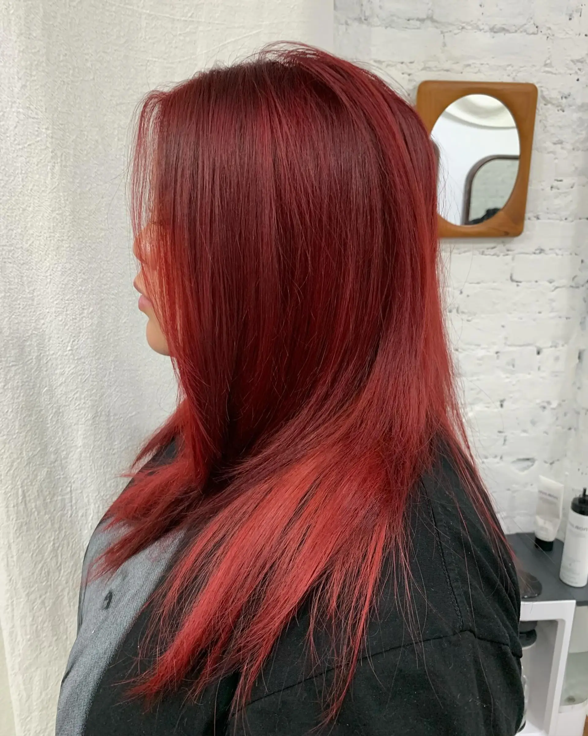 A long, straight, vibrant red hairstyle with layered cuts, styled with a side part for a sleek look. 1