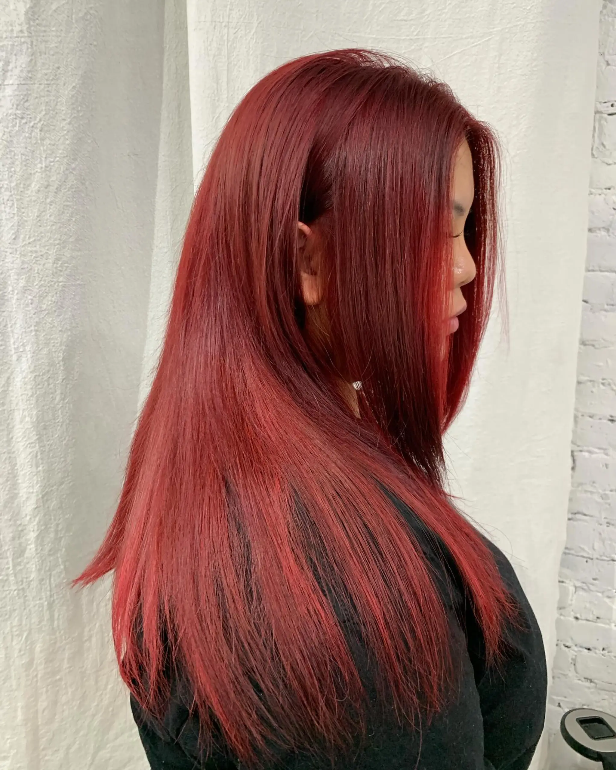 A long, straight, vibrant red hairstyle with layered cuts, styled with a side part for a sleek look. 2