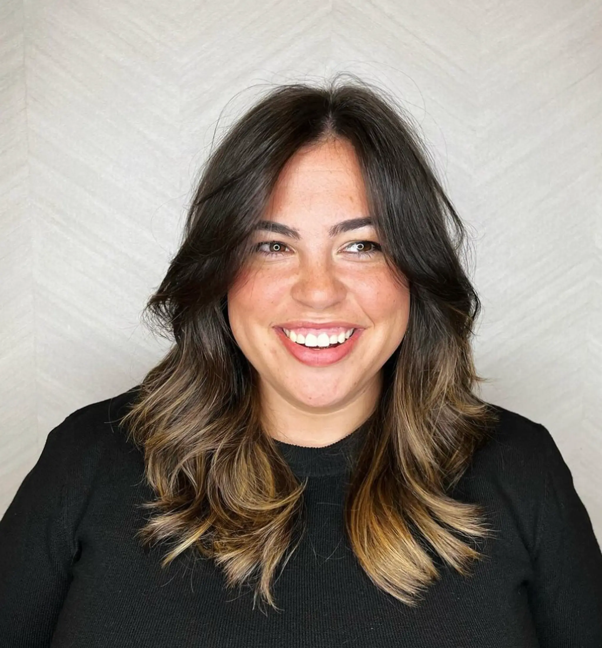 A layered, wavy hairstyle with long locks and a subtle ombre effect from dark brown to blonde highlights, featuring natural waves and face-framing layers.

Cut and style by @juliamannino_hair
