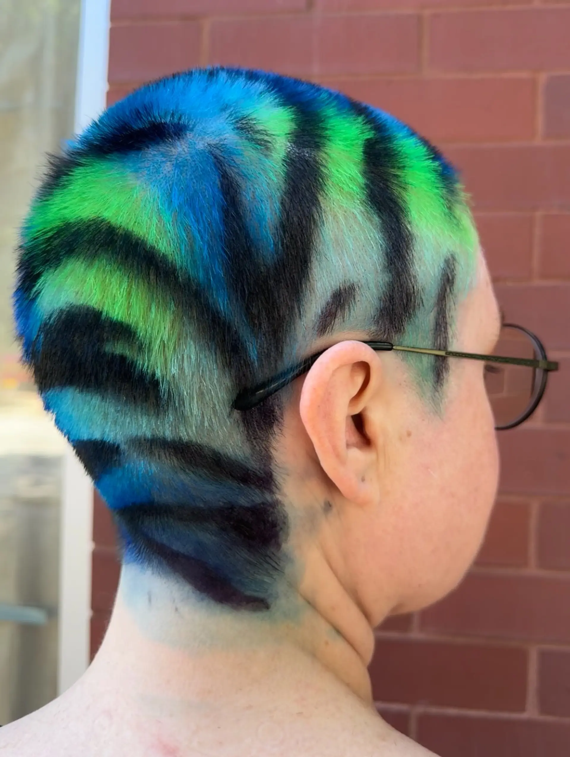 A close buzz cut featuring vibrant green and blue vivid hair color with bold, hand-painted black tiger stripes. 1