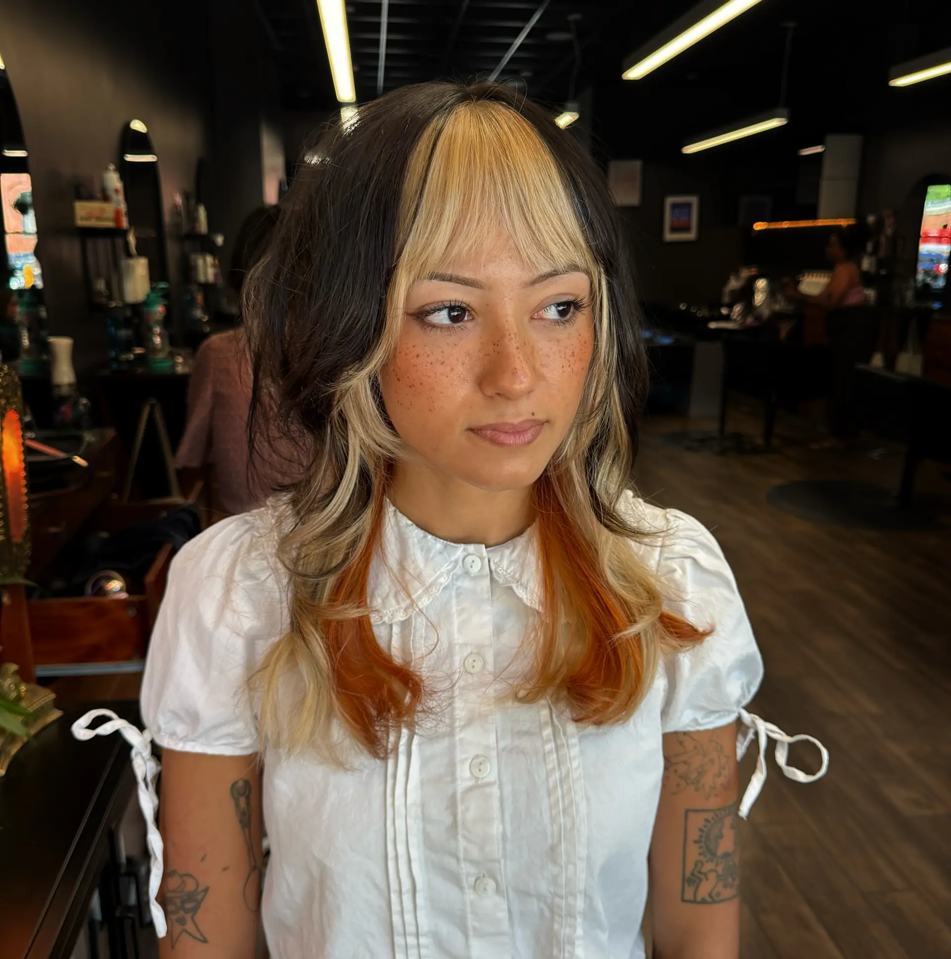 A textured mid-length shag cut featuring blunt blonde bangs, dark brown layers, and vibrant copper peekaboo underlights. 1