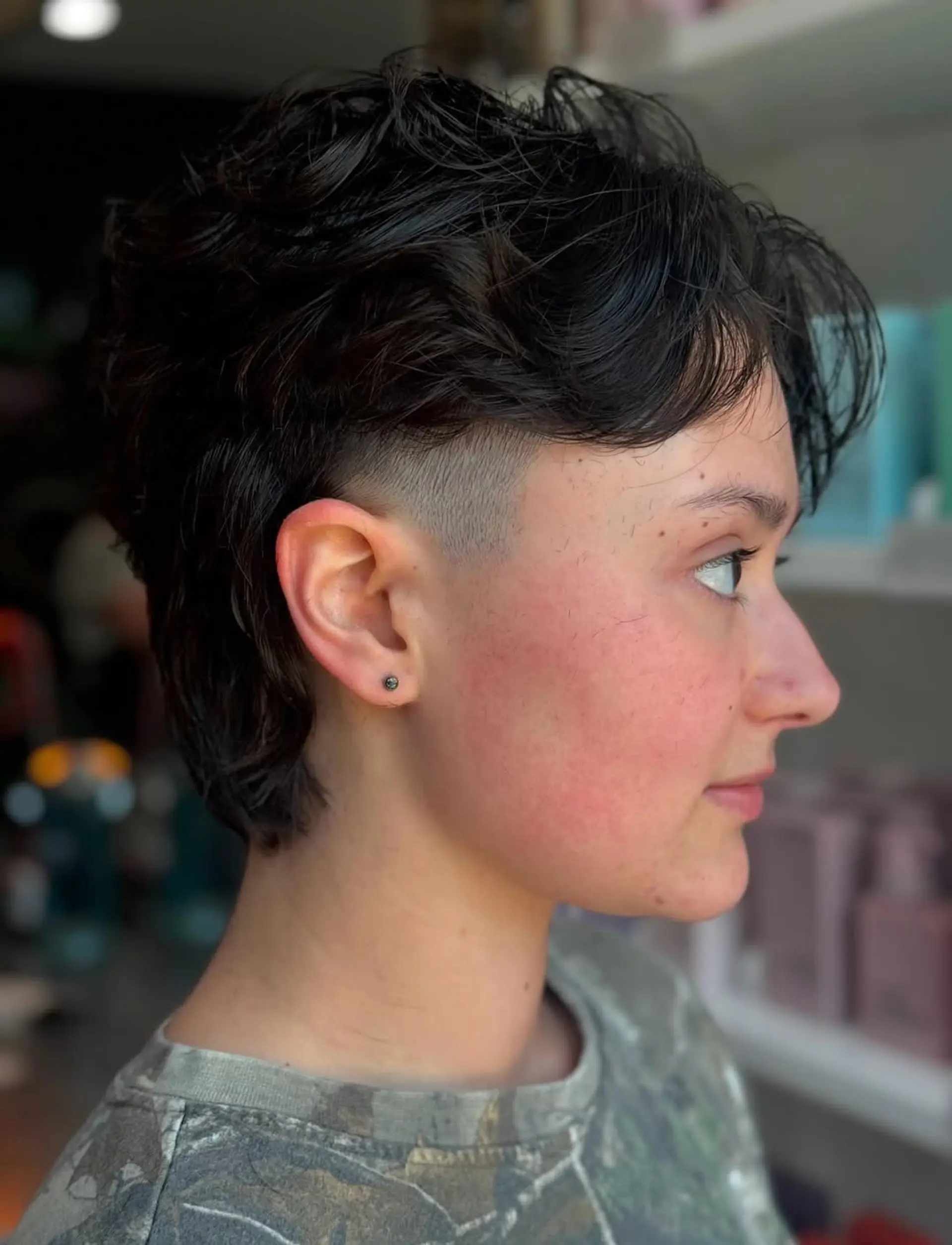 An edgy modern undercut mullet with textured wavy dark hair. The sides are faded short, while the top and back maintain medium-length waves for volume and a contemporary shag feel. 1