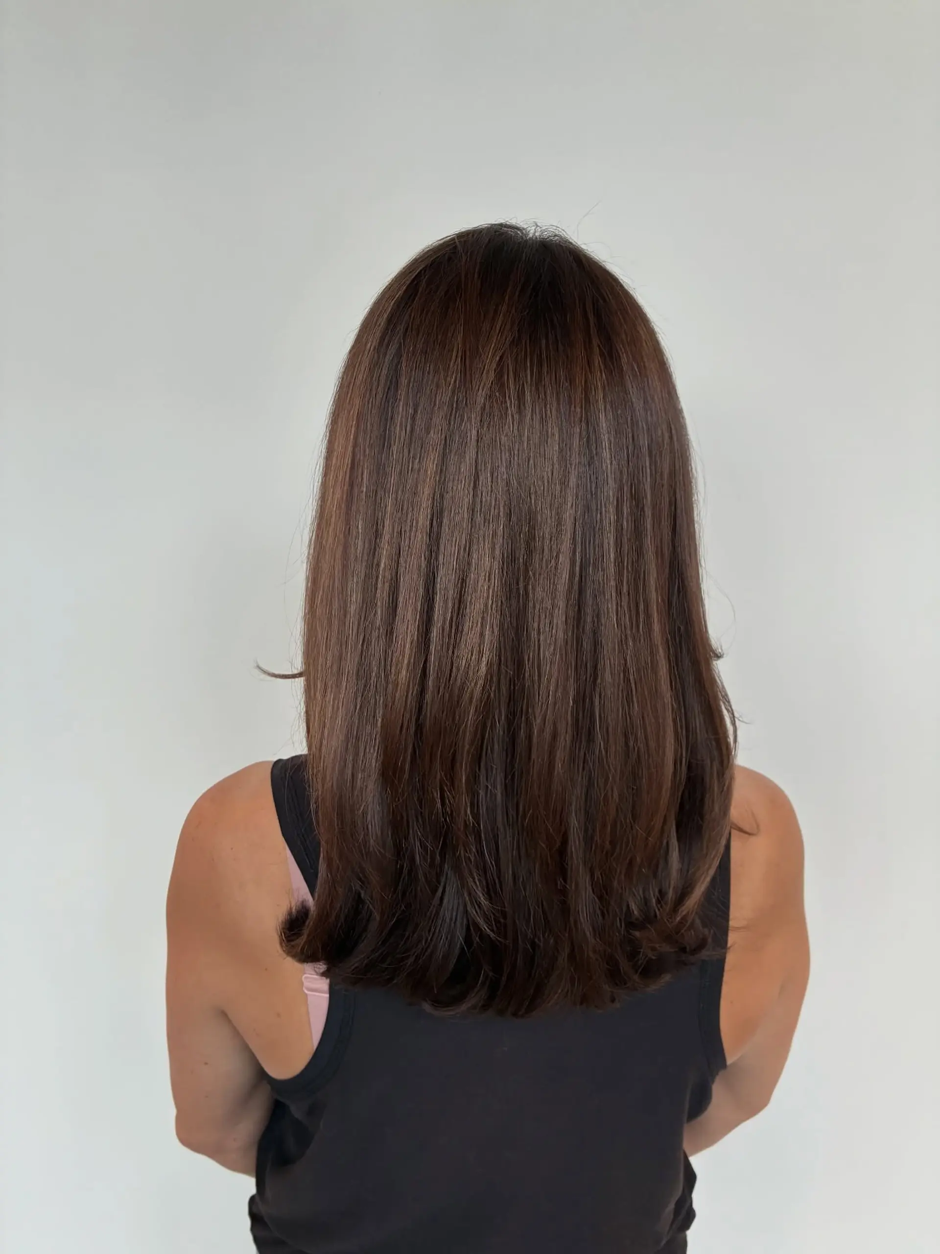 Rich brunette hair featuring soft dimensional highlights, styled into a smooth and polished blowout with gentle inward curls at the ends. 1