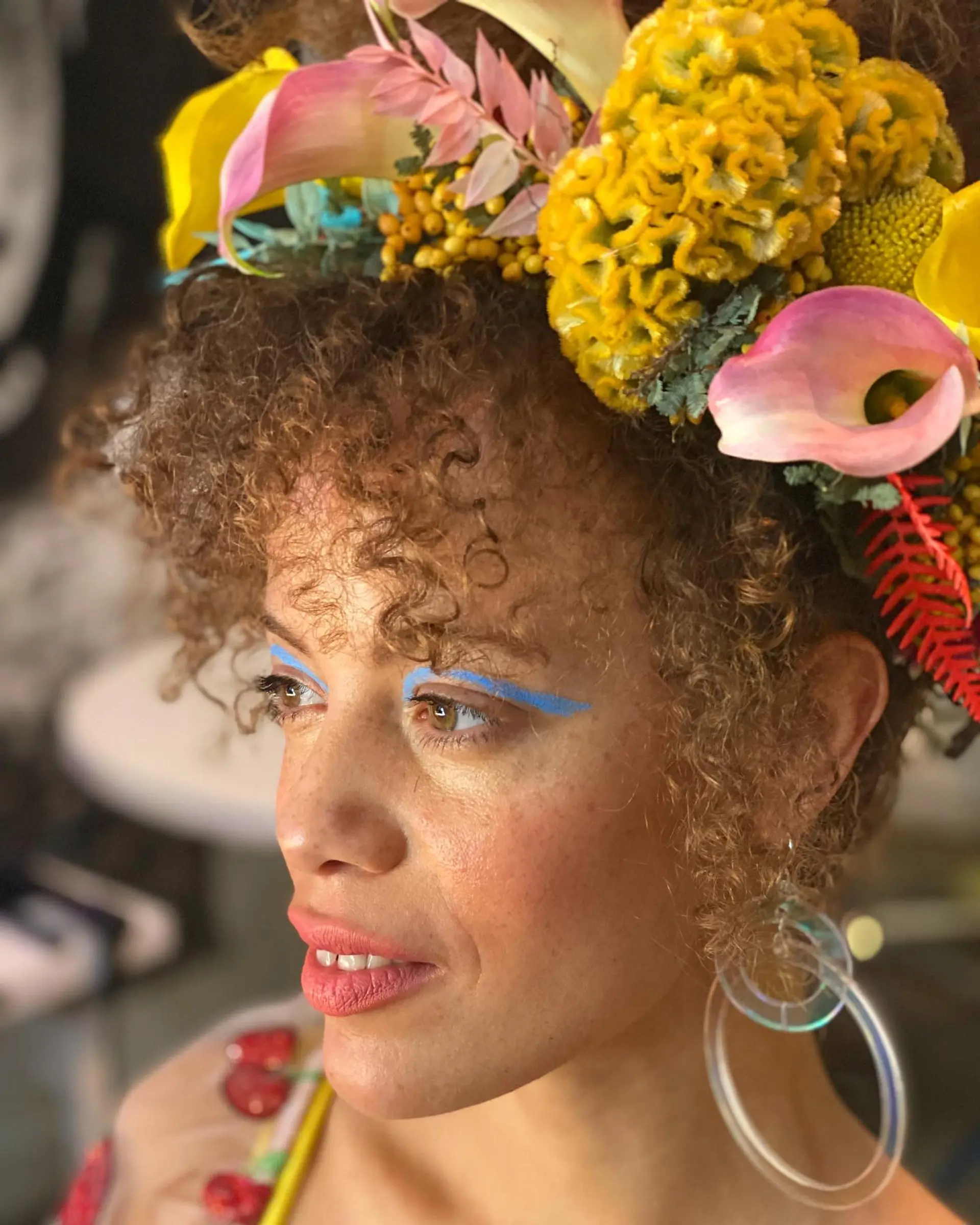 Naturally curly hair styled into an updo topped with an extravagant floral headpiece, accented by soft curly fringe. 1