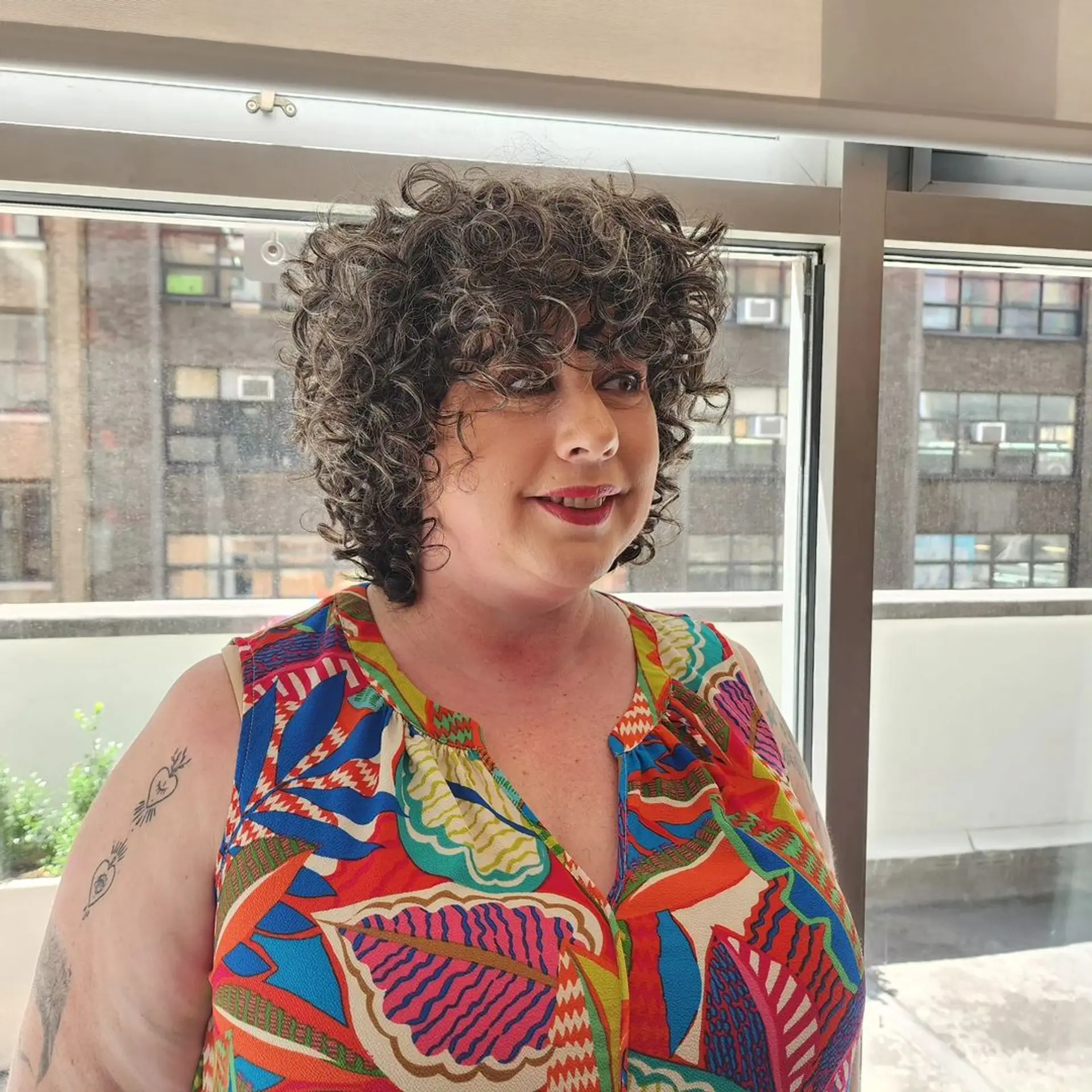 A short curly bob with dark brown hair and gray highlights, featuring natural, voluminous curls and layers for added bounce. 2