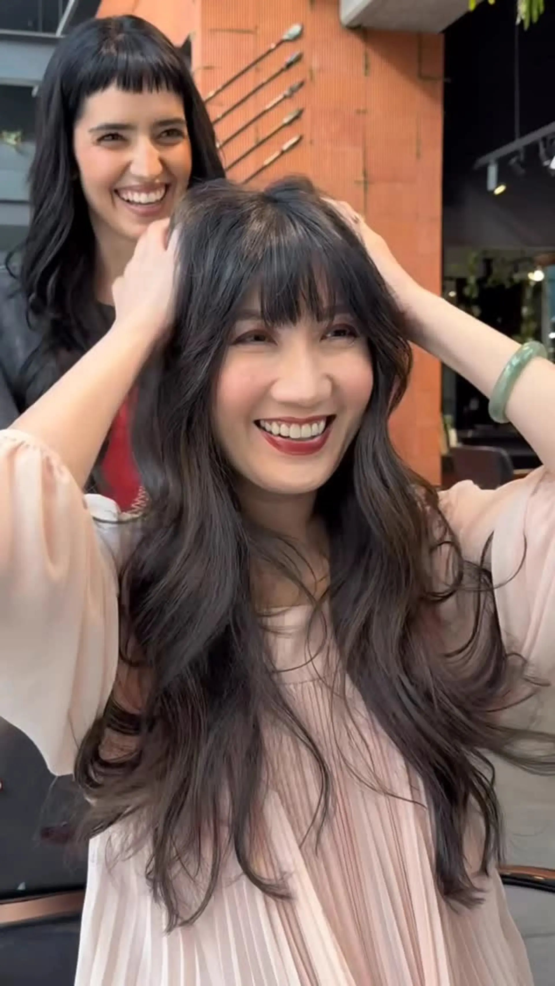 Long dark brunette hair cut with soft, airy layers and styled in voluminous waves, complemented by eyebrow-skimming bangs. 1
