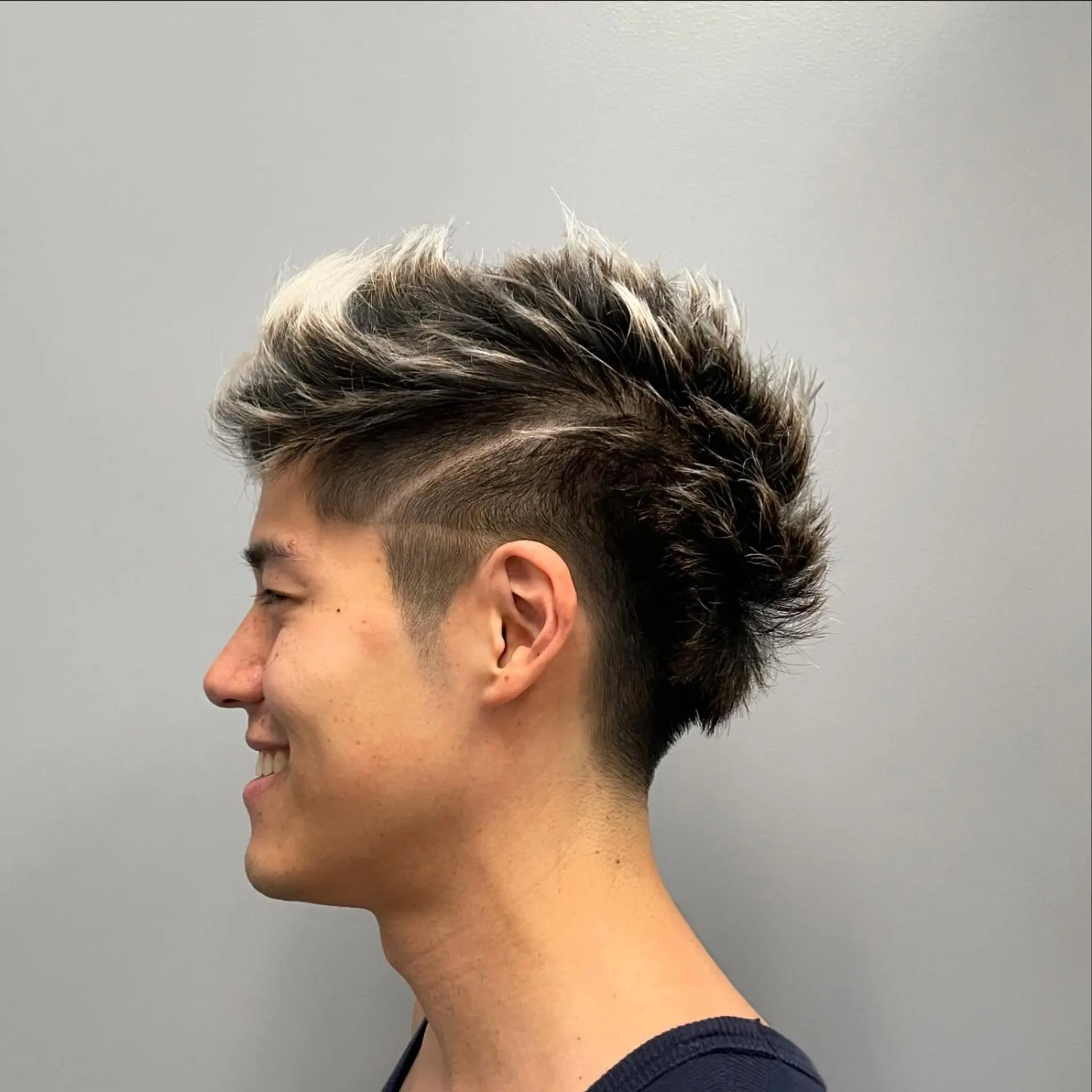 A modern textured faux hawk haircut featuring short faded sides, a shaved accent line, and heavily textured, spiky top sections with frosted blonde tips. 1