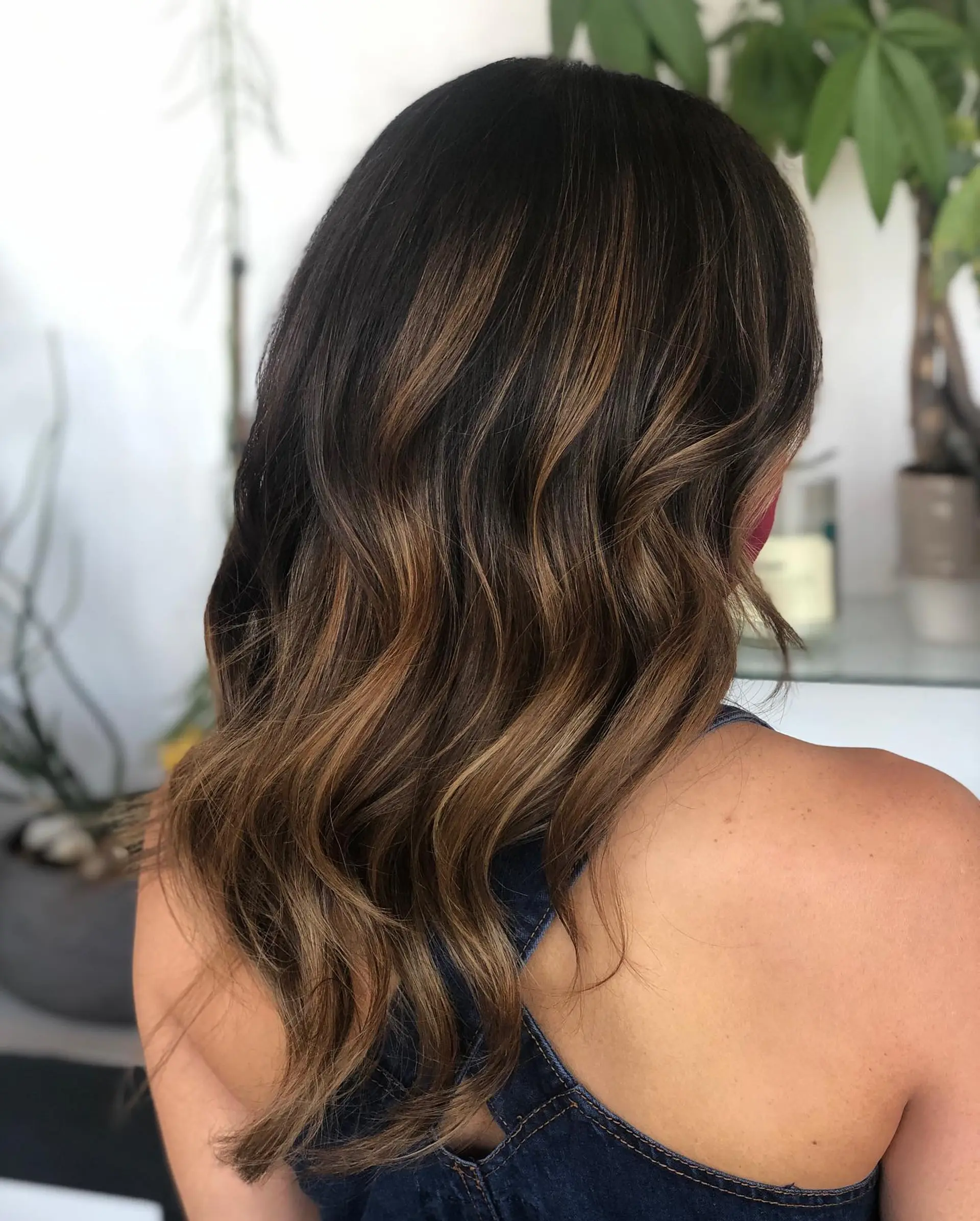 Rich dark brunette hair enhanced with dimensional caramel balayage and subtle highlights, styled into soft loose waves. 1