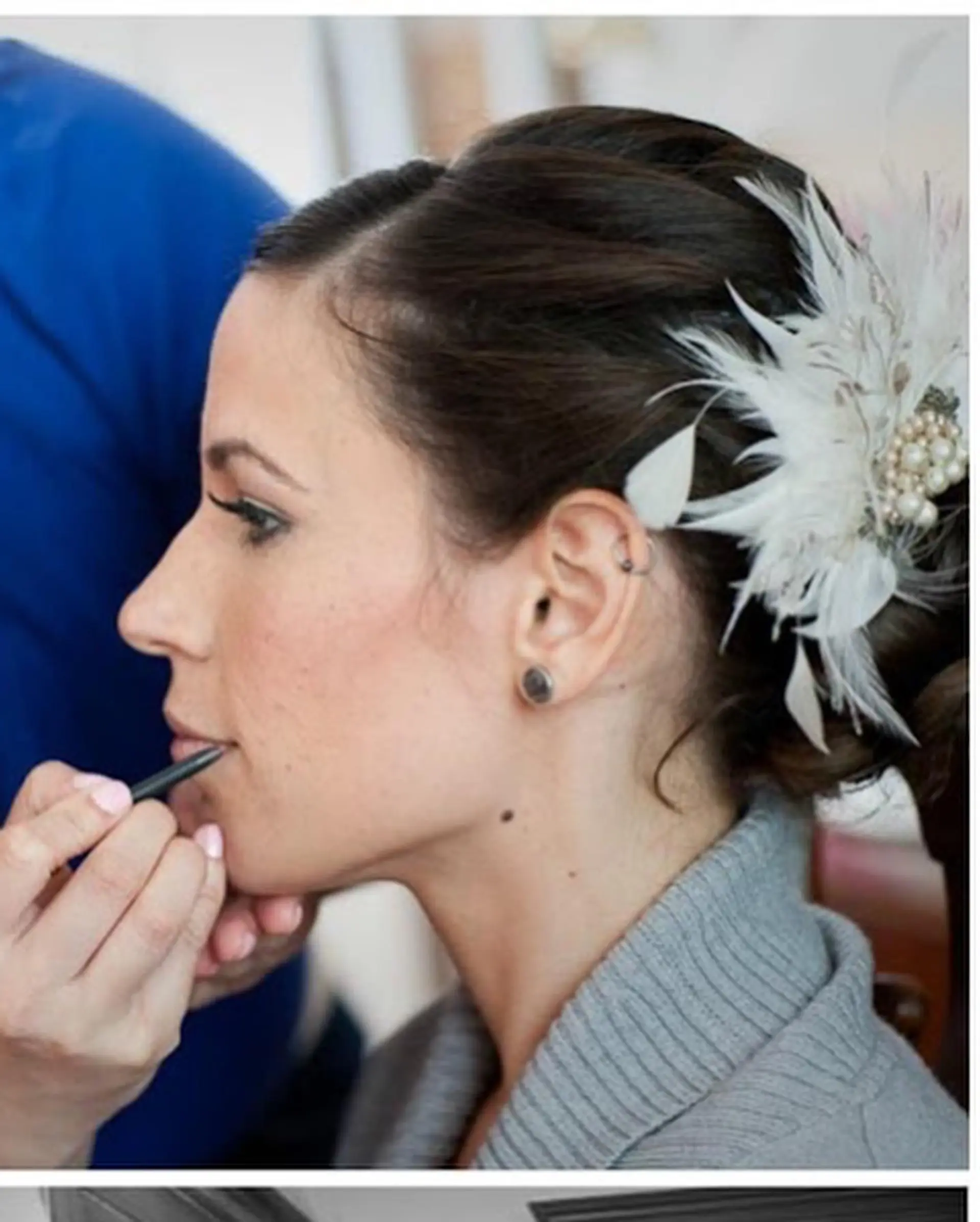 An elegant bridal updo adorned with a white feather and pearl hairpiece. 1