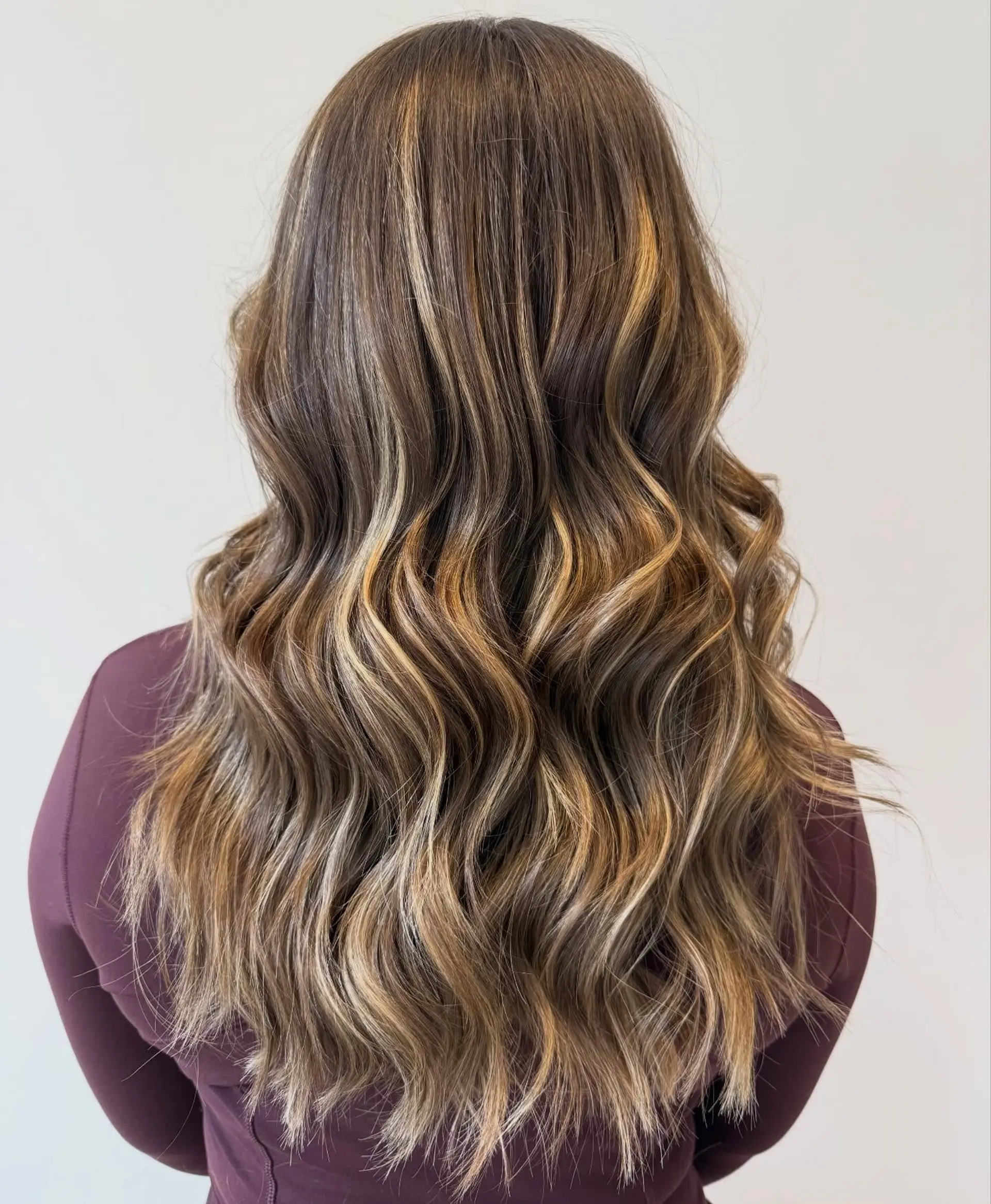 Long dark brown hair with warm honey blonde balayage highlights styled in soft, loose waves. 1