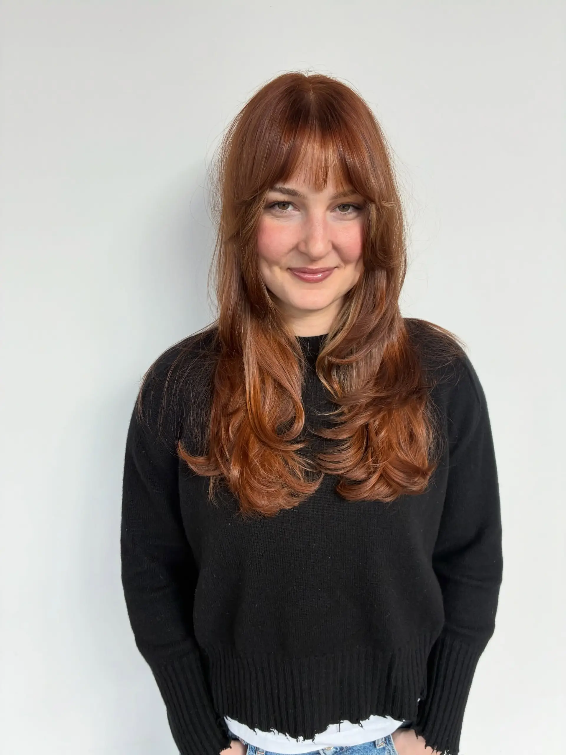Long deep copper hair styled with soft, face-framing layers, wispy bangs, and gently curled, bouncy ends. 1