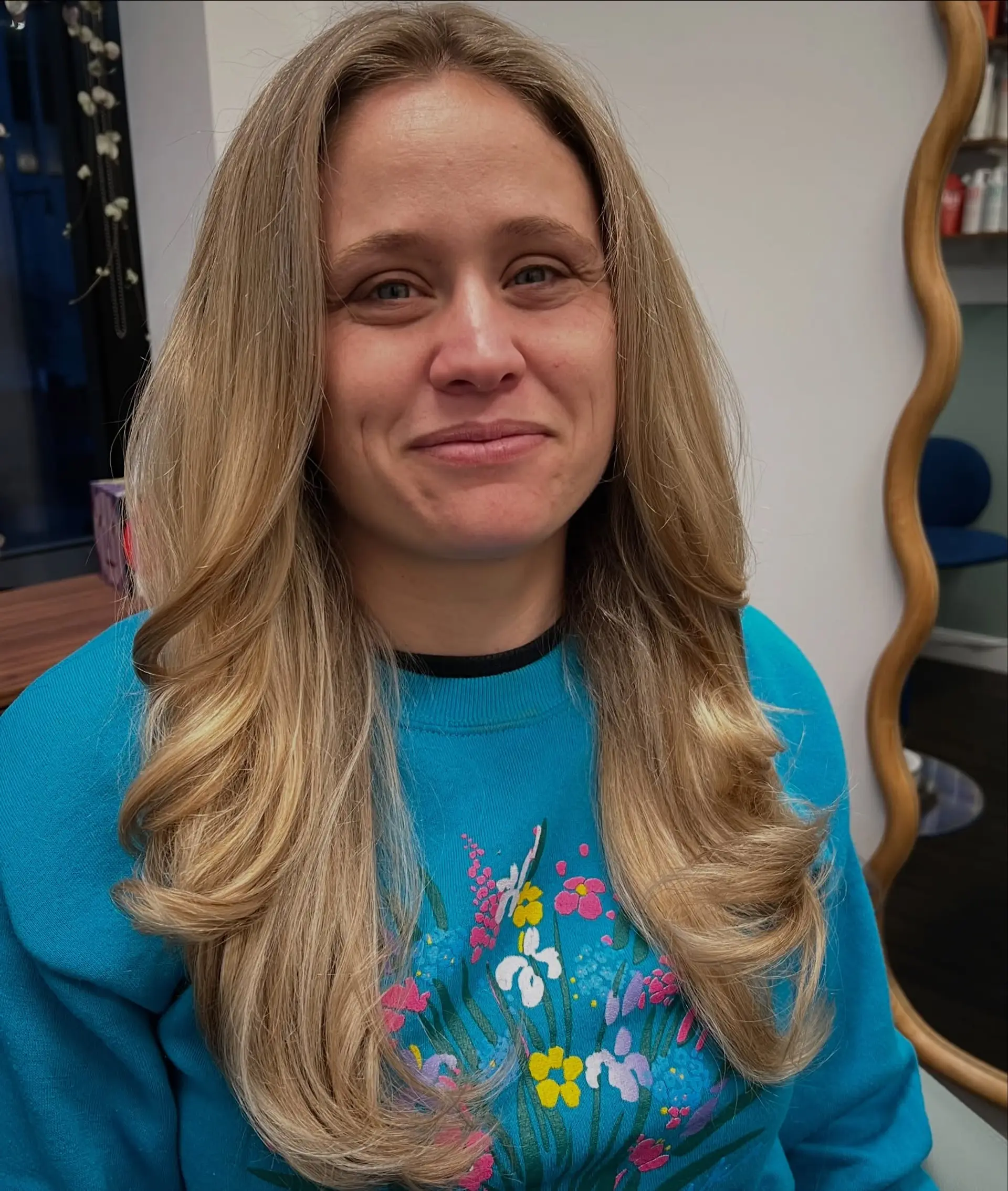 Long warm blonde hair cut with face-framing layers and styled in a bouncy, voluminous blowout with flipped curled ends. 1