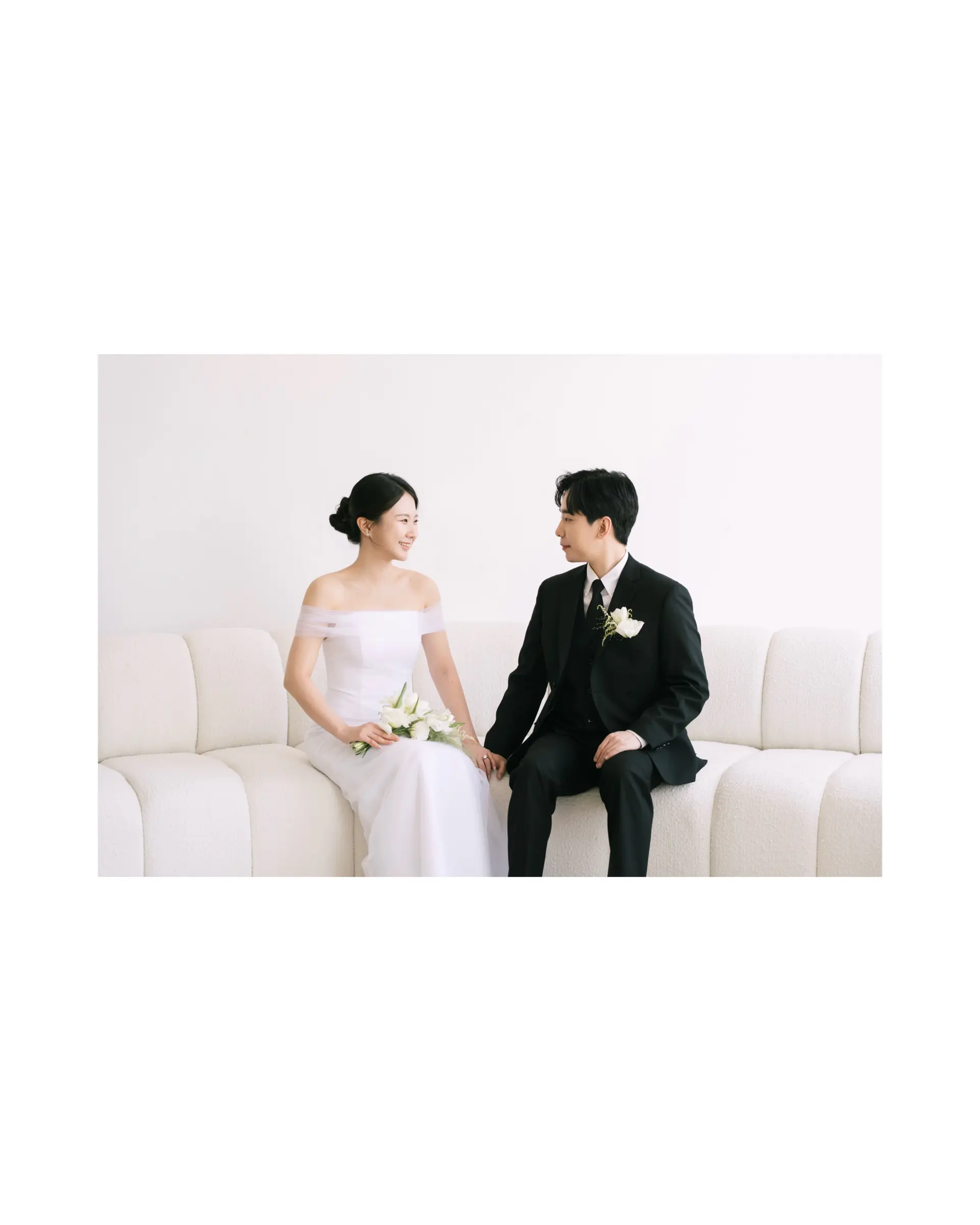 A clean, elegant low bridal bun paired with polished, neatly parted groom styling for a studio photoshoot. 1