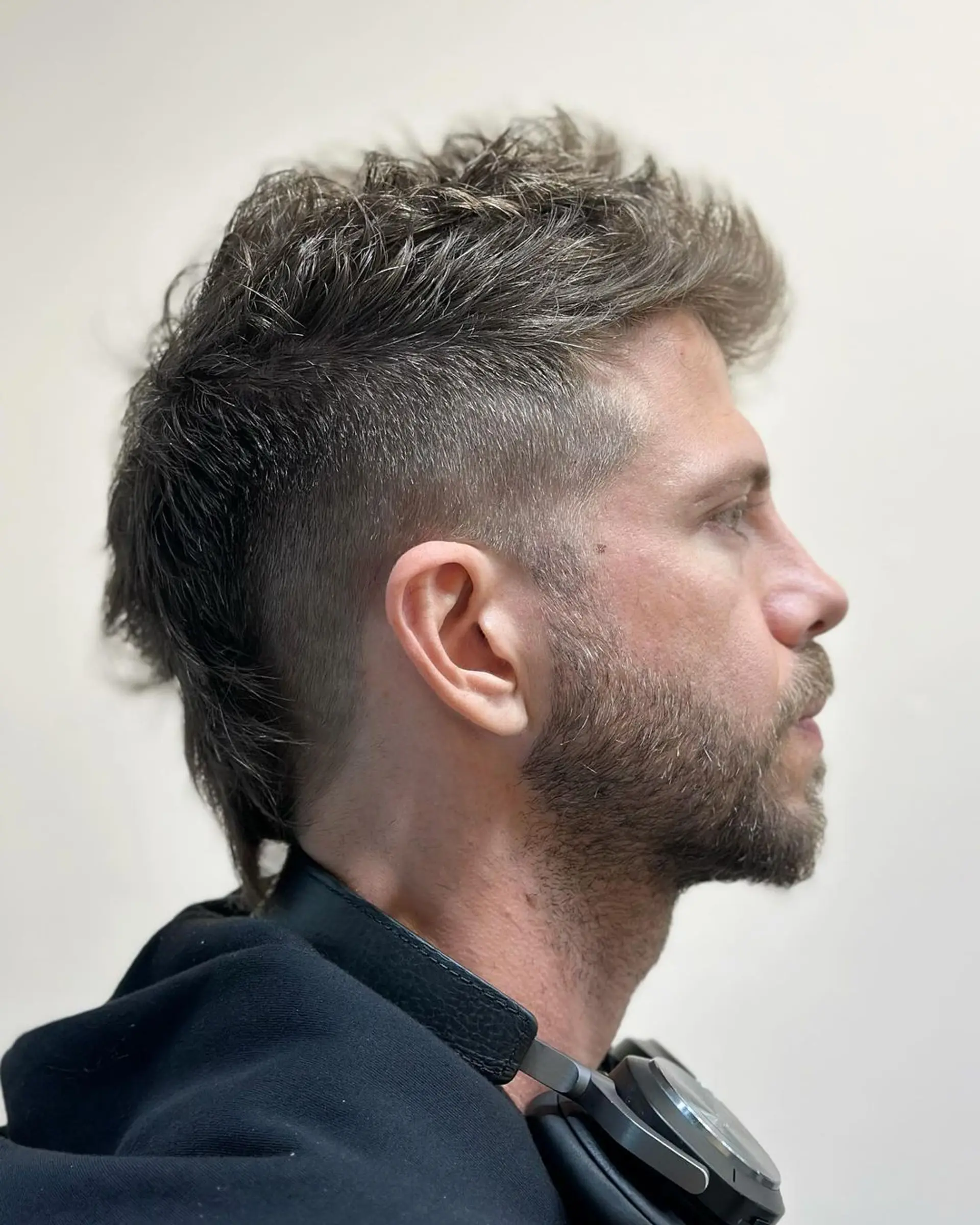 An edgy, textured mohawk with a high fade, featuring dark brown, wavy hair with significant volume on top and subtle tapering at the back. 2