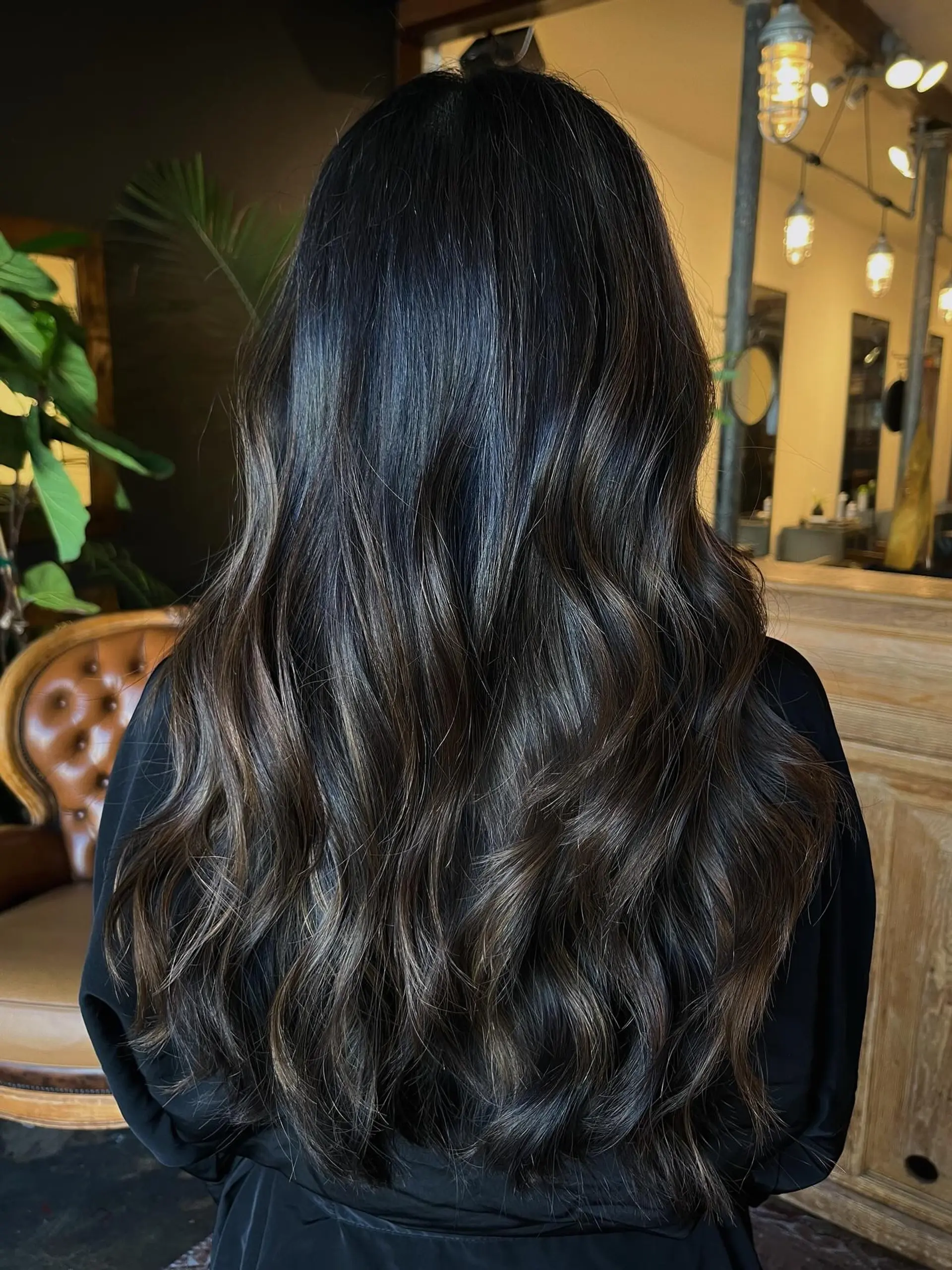 Long, deep espresso brunette hair with subtle dimensional babylights styled into soft cascading waves. 1