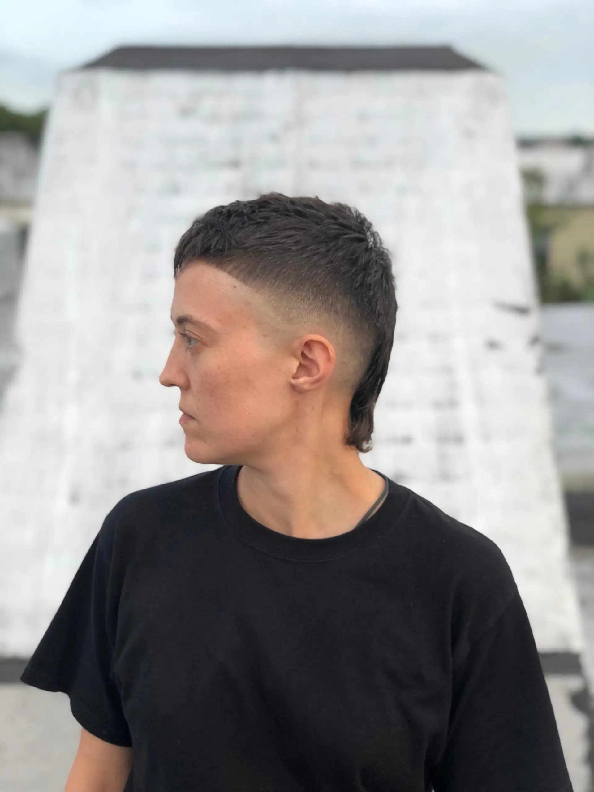A modern cropped mullet featuring a tight skin fade around the temples and ears, textured blunt micro-bangs, and extended length down the nape. 1