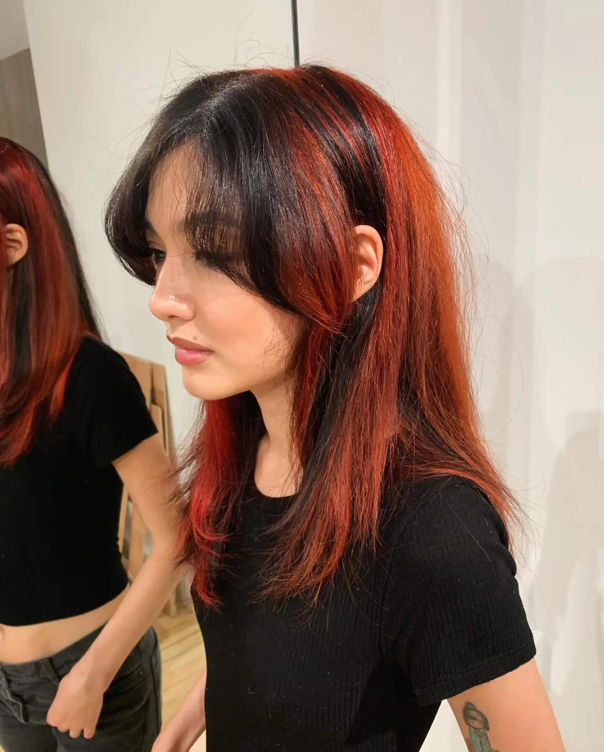 A long, straight hairstyle featuring bold black and red hues. It is accented with soft layers and fringe bangs, offering a striking and elegant contrast. 2