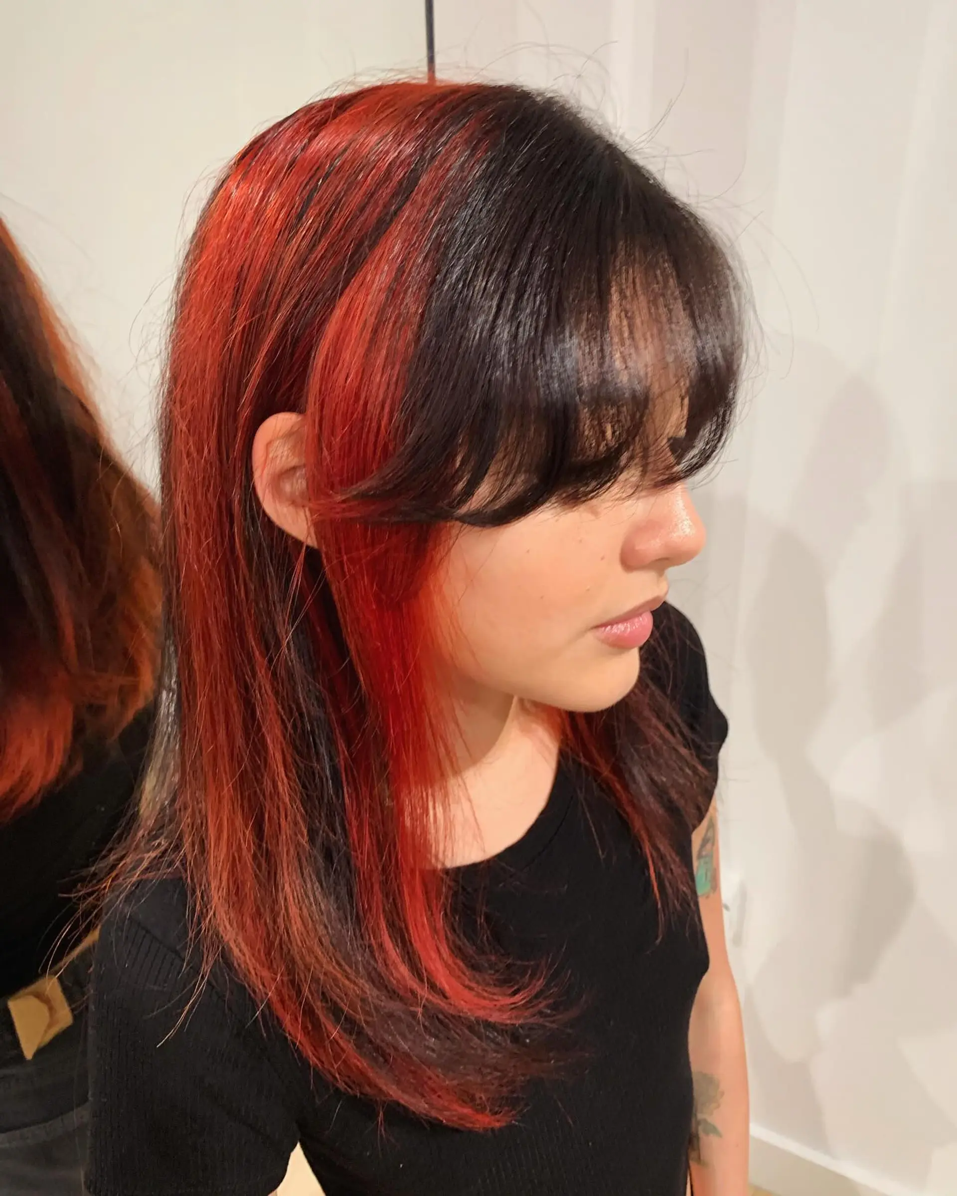 A long, straight hairstyle featuring bold black and red hues. It is accented with soft layers and fringe bangs, offering a striking and elegant contrast. 3