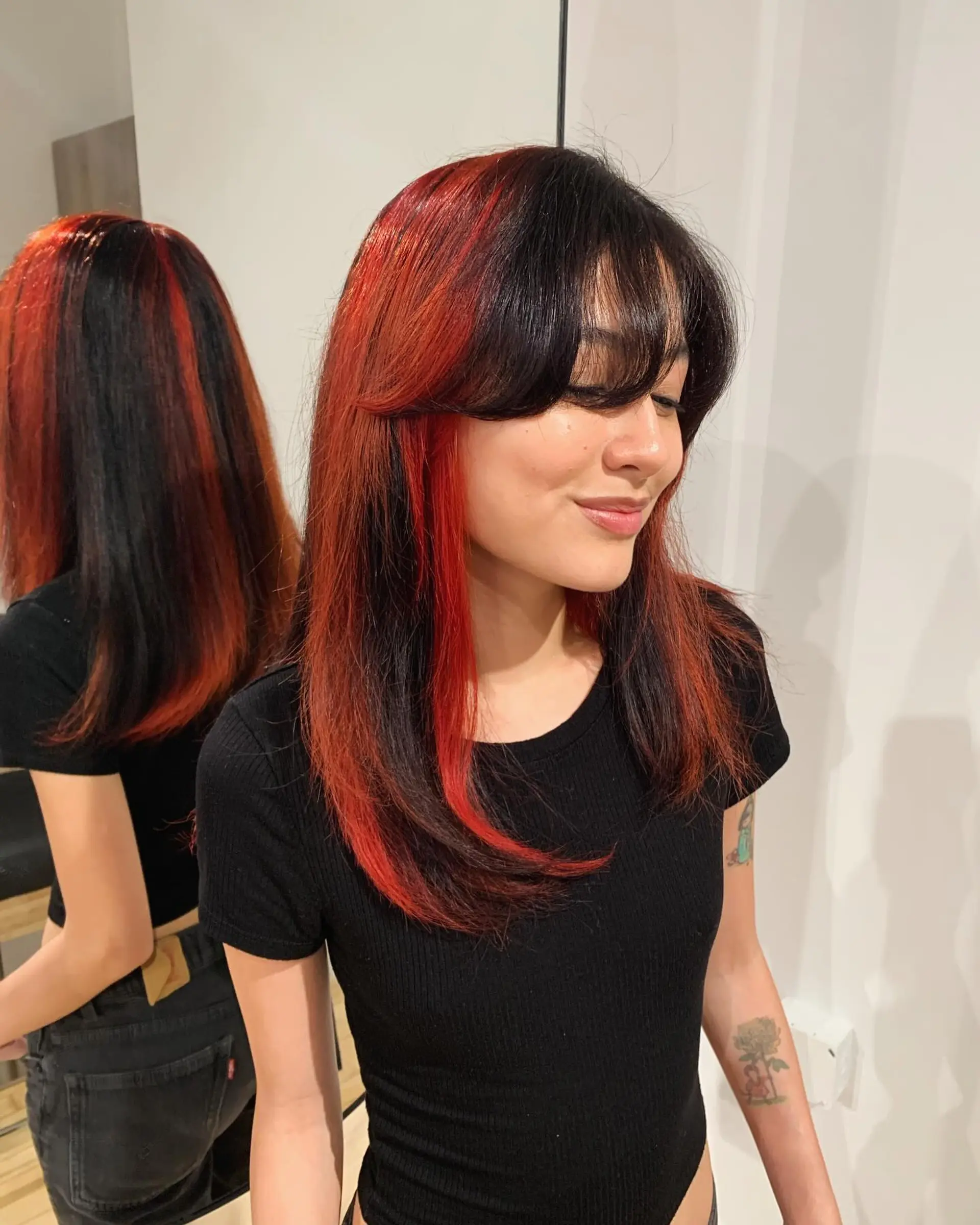 A long, straight hairstyle featuring bold black and red hues. It is accented with soft layers and fringe bangs, offering a striking and elegant contrast. 4