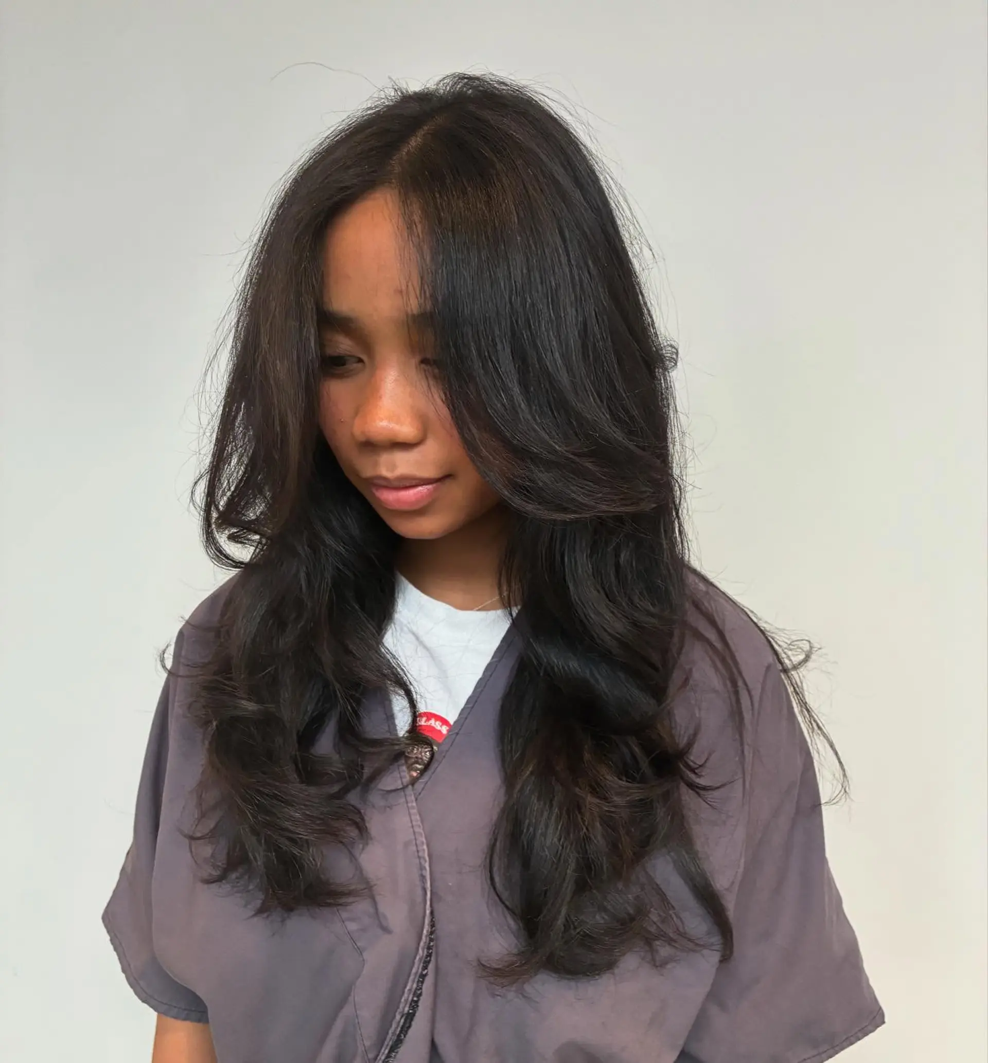 Long, layered dark hair styled into a soft, voluminous blowout with bouncy ends and face-framing curtain layers. 1