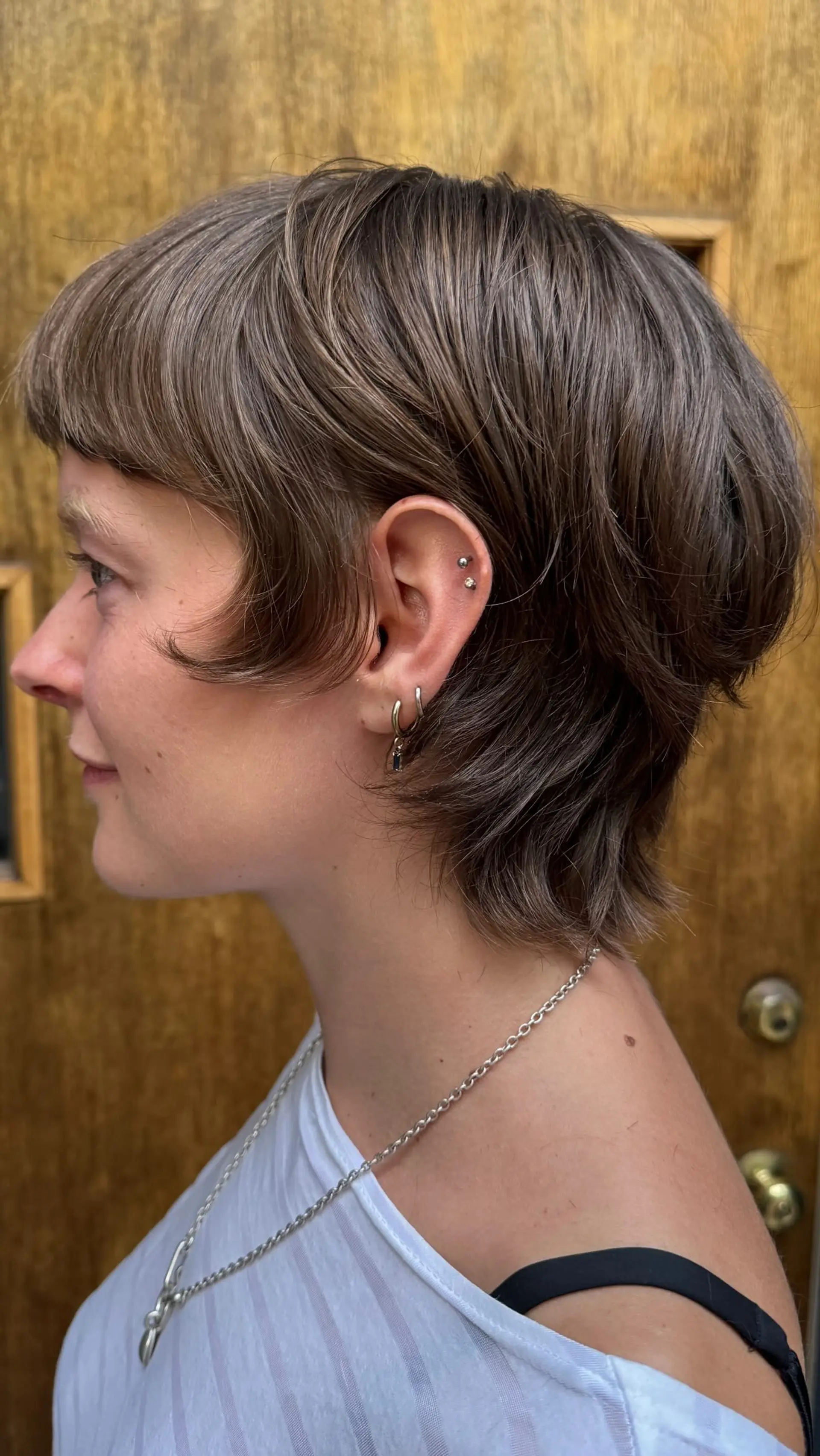 A textured razor-cut bixie featuring soft feathered layers, micro blunt bangs, and light wisps framing the ears and nape. 1