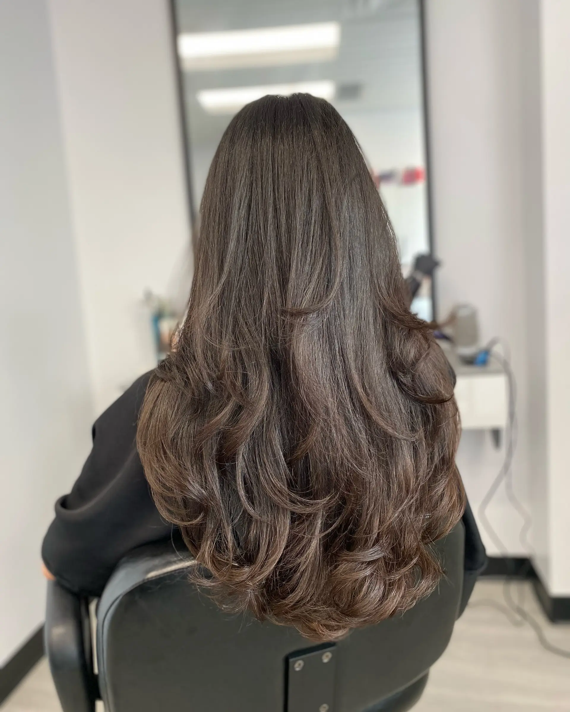 Long, dark brunette hair featuring multi-tiered layers styled into a soft, bouncy blowout with curled ends. 1