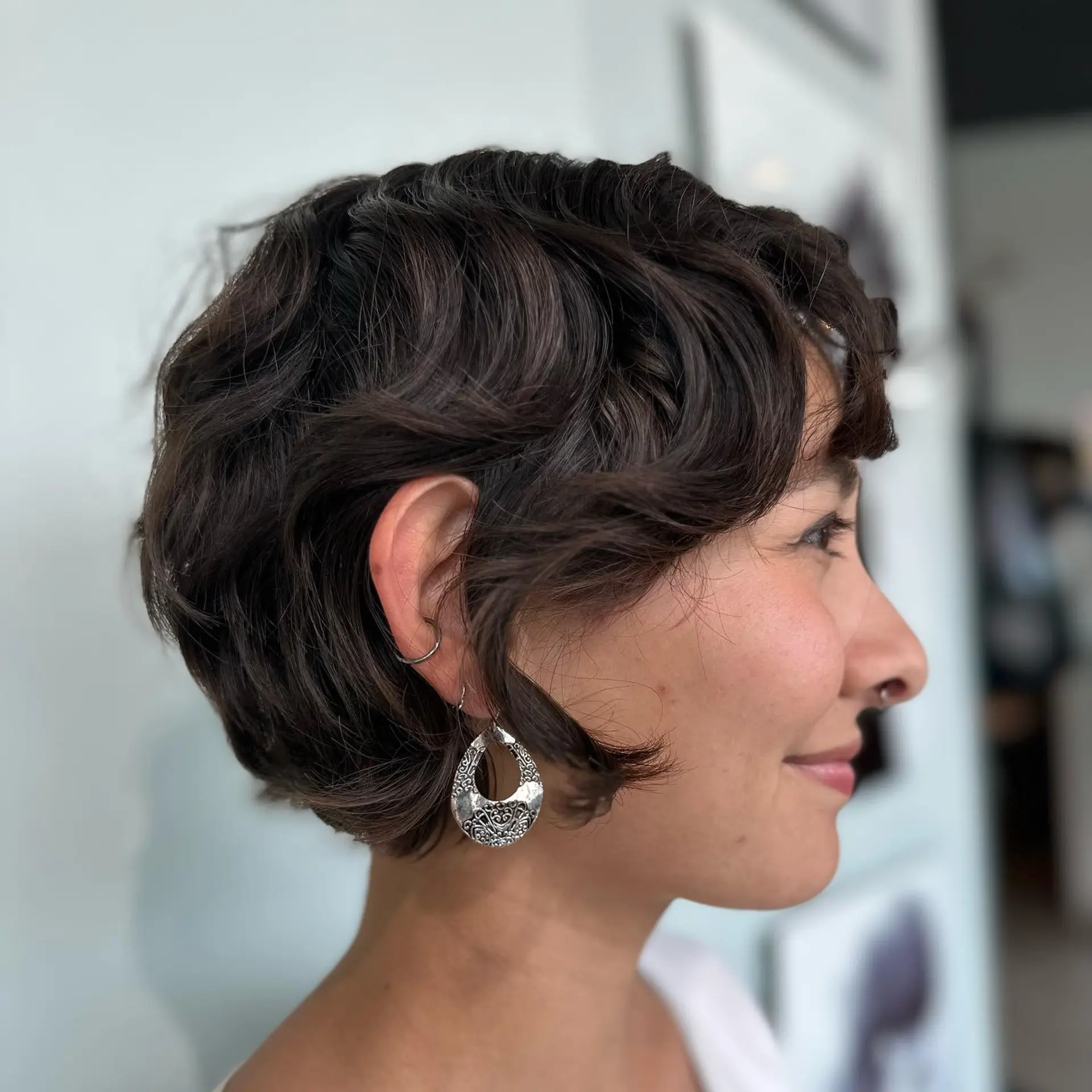 A textured dark brown bixie haircut styled with soft waves and subtle face-framing fringe. 1