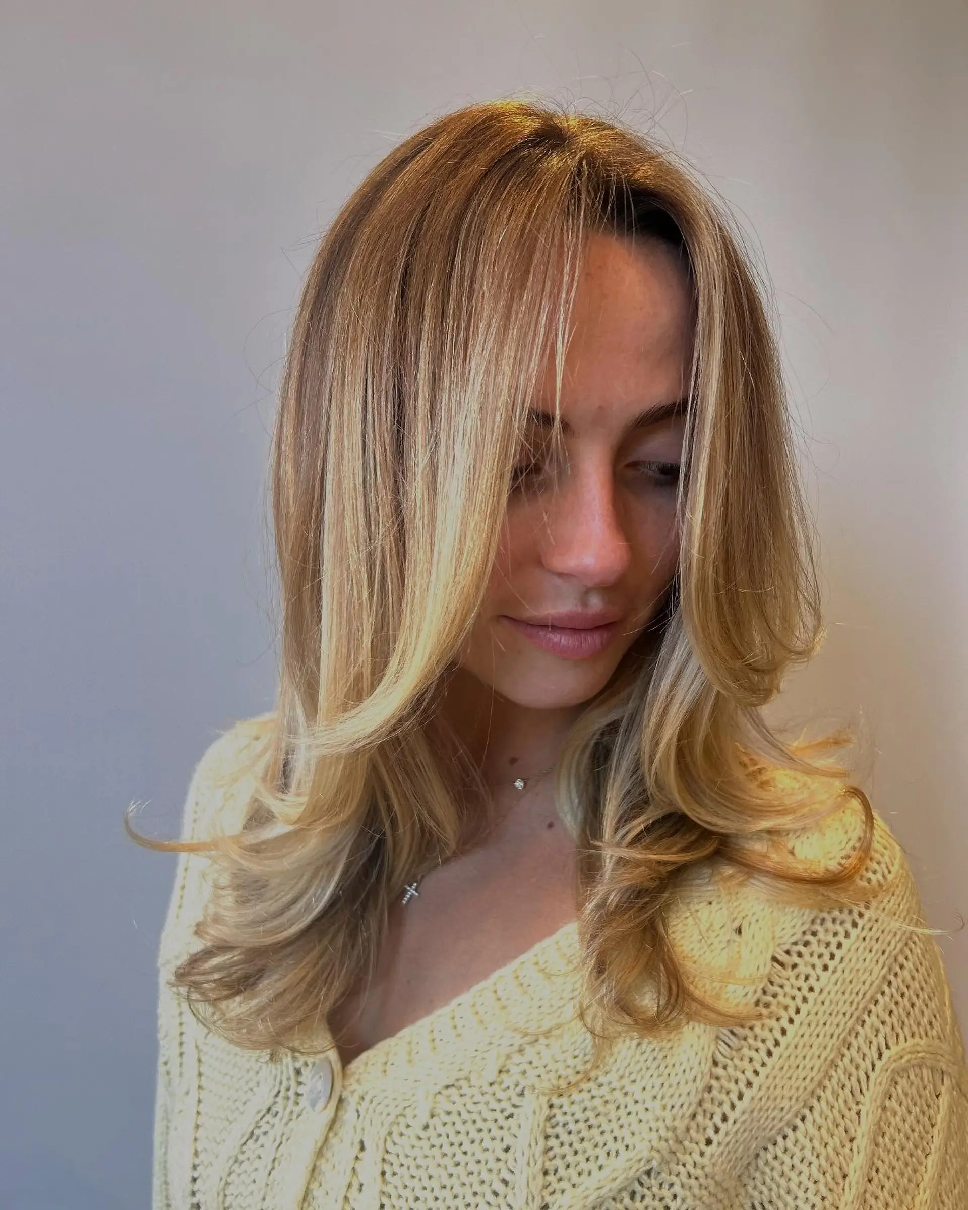 Medium-length layered blonde hair styled with face-framing curtain layers and softly curled, bouncy ends. 1