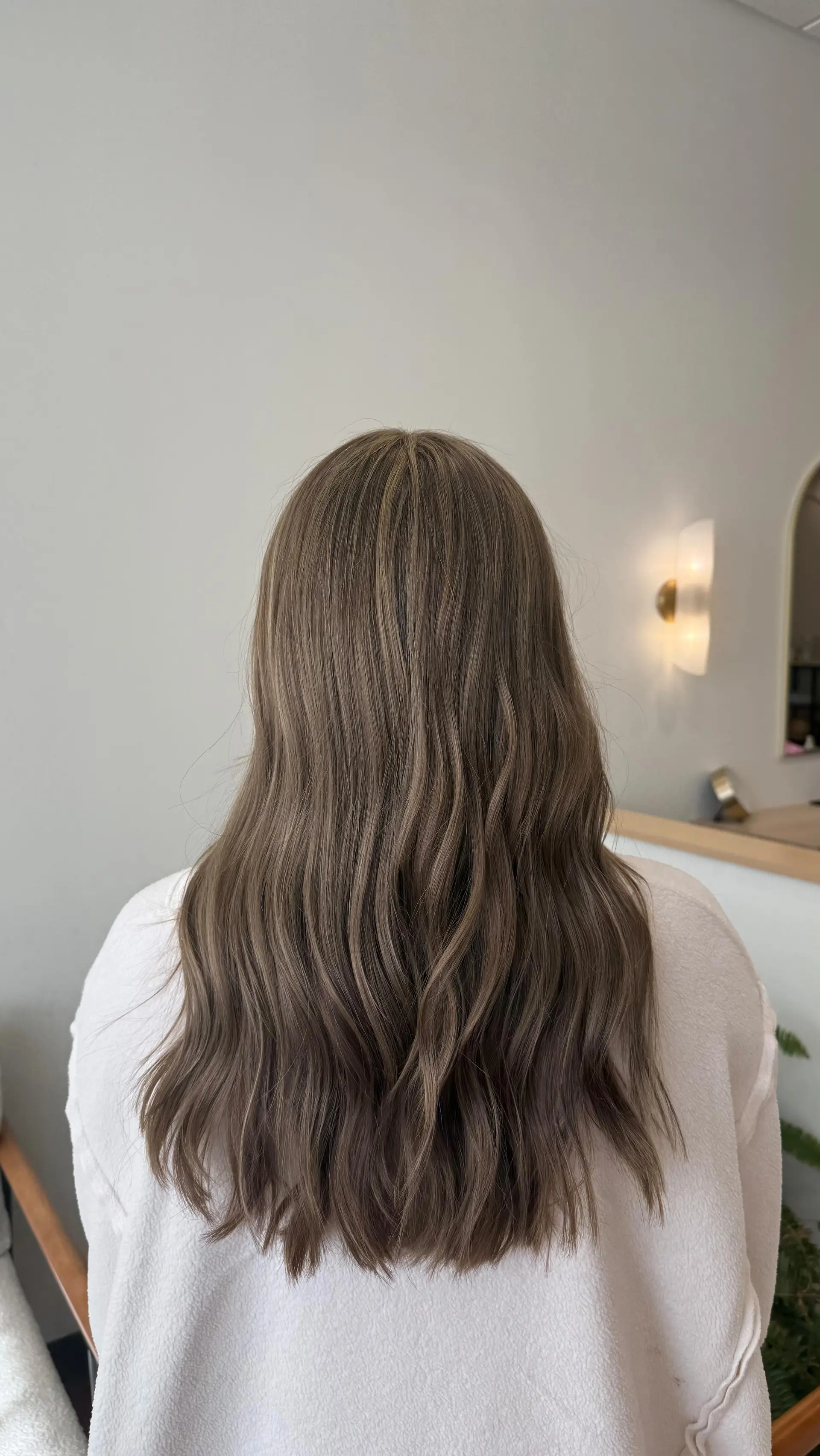 Long ash-toned dimensional brunette hair styled in loose, gentle waves cascading down the back. 1