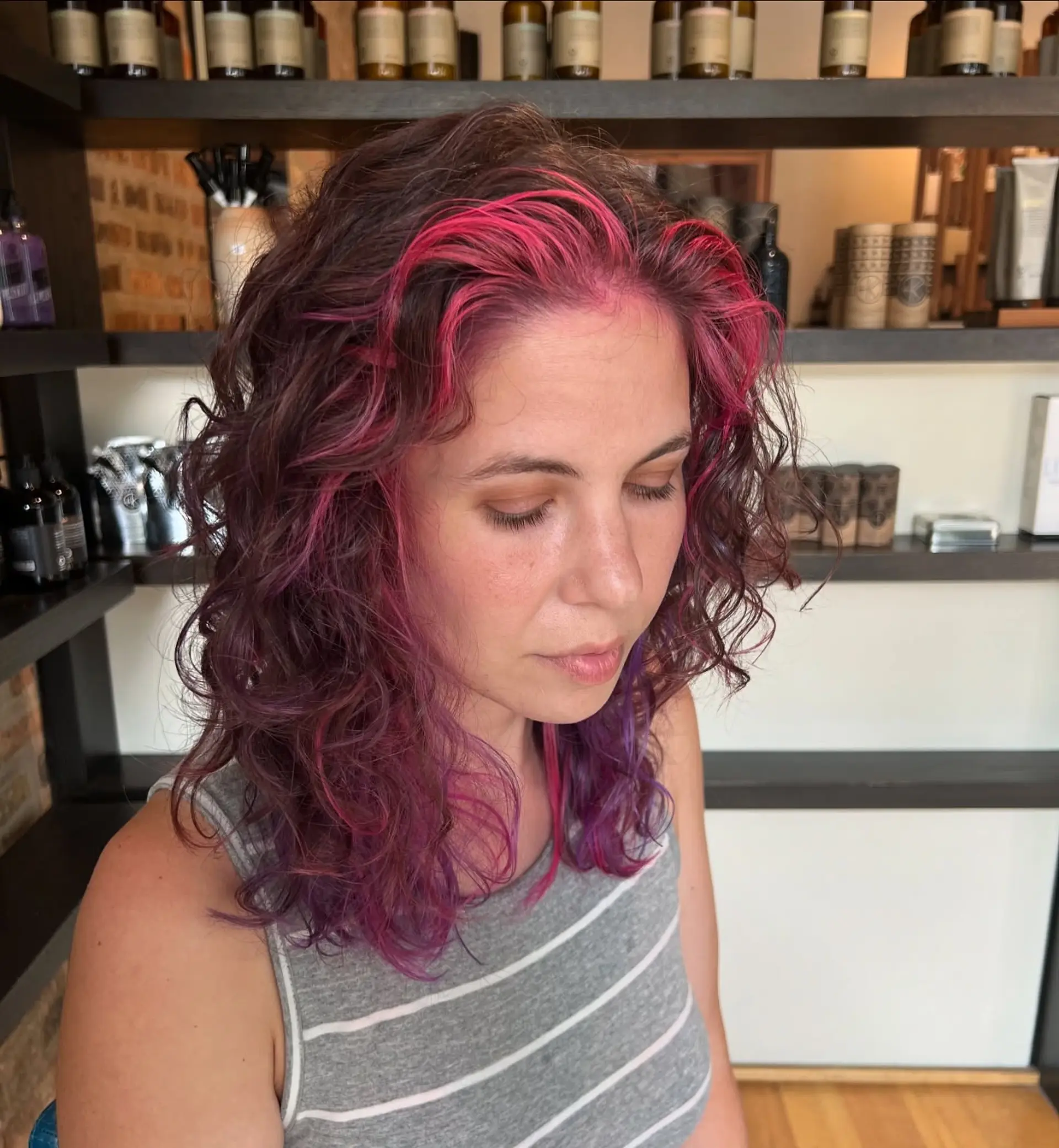 Medium curly hairstyle with playful crimson, pink, and purple balayage highlights. 1