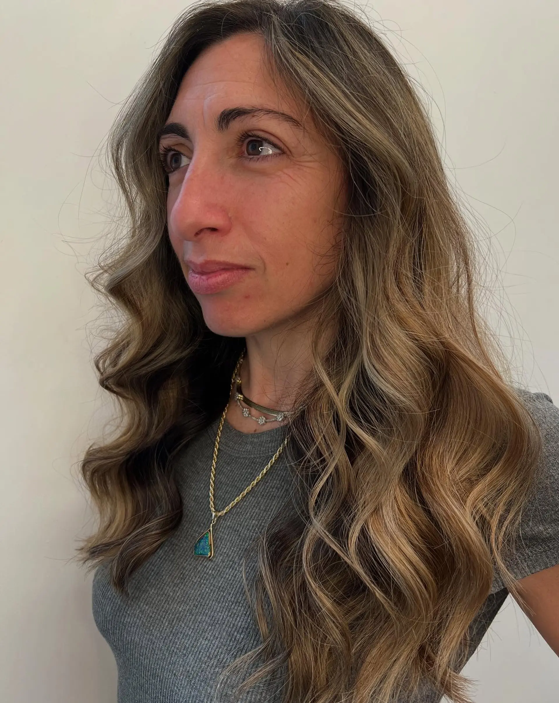 Long hair styled into polished, soft waves with warm sun-kissed balayage highlights seamlessly blended through the mid-lengths and ends. 1