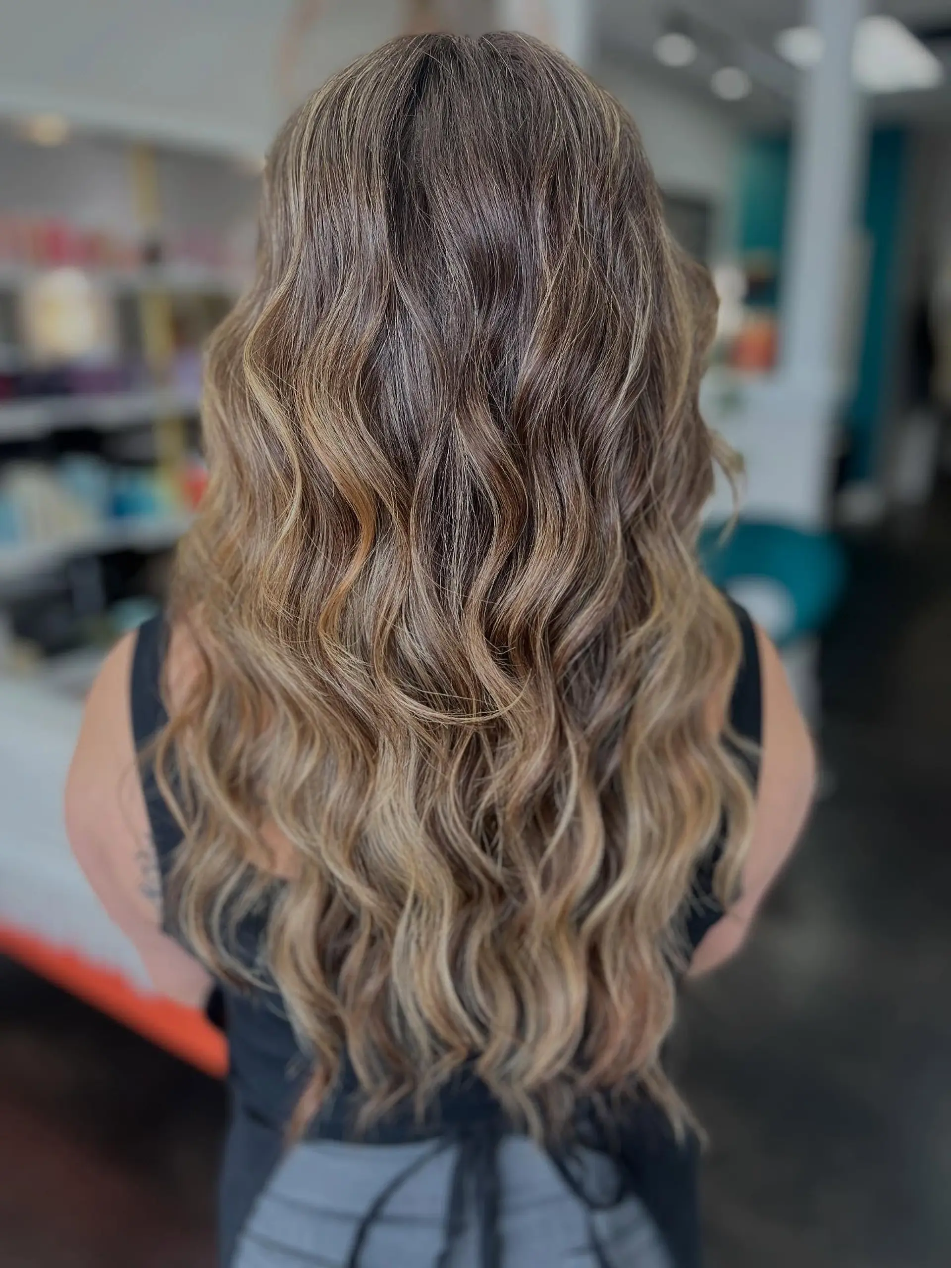 Long cascading waves featuring a seamless, natural sun-kissed blonde balayage over a soft brown base. 1
