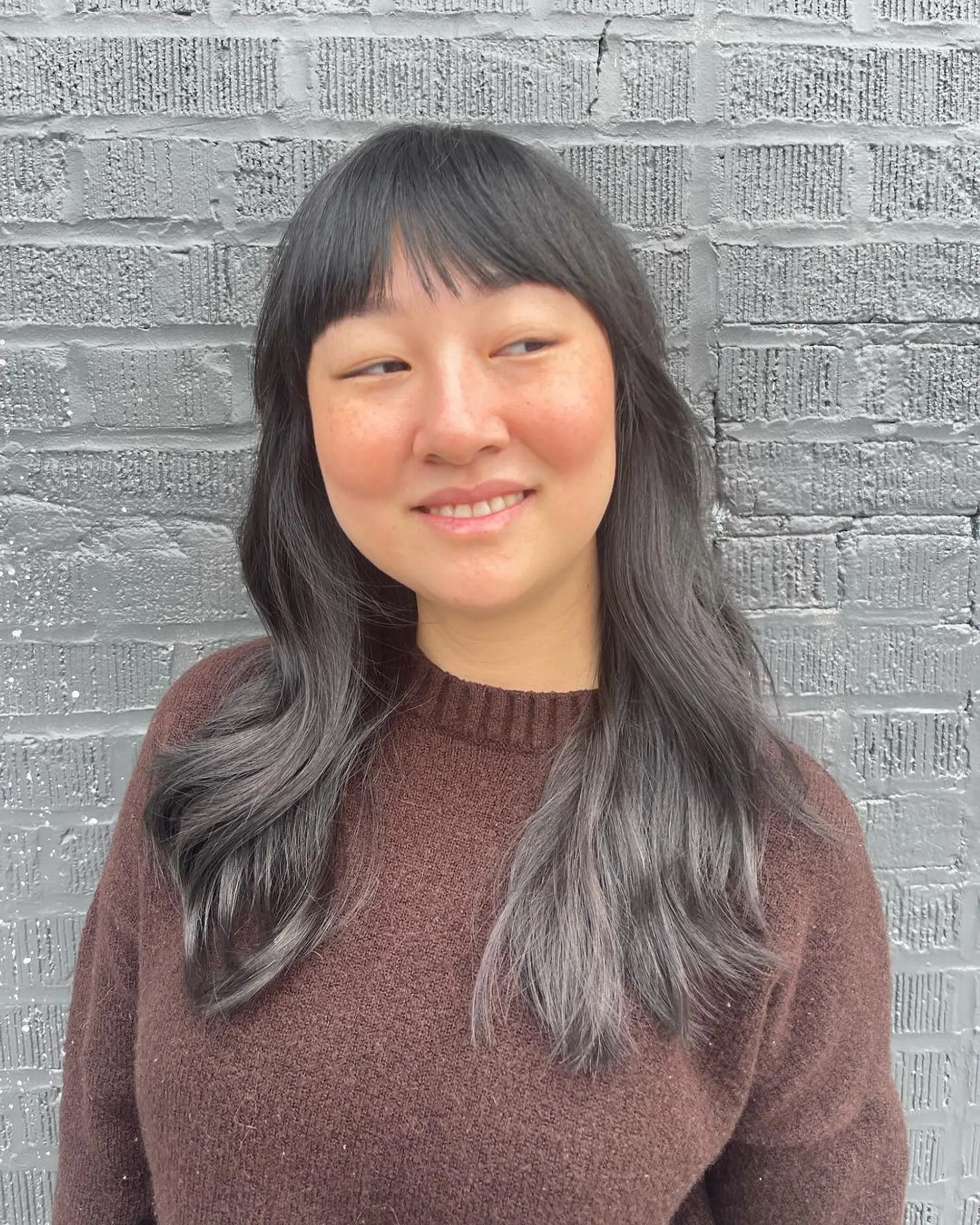 Long, wavy hairstyle with black and gray tones, featuring soft bangs and layered ends for a casual, elegant appearance. 1