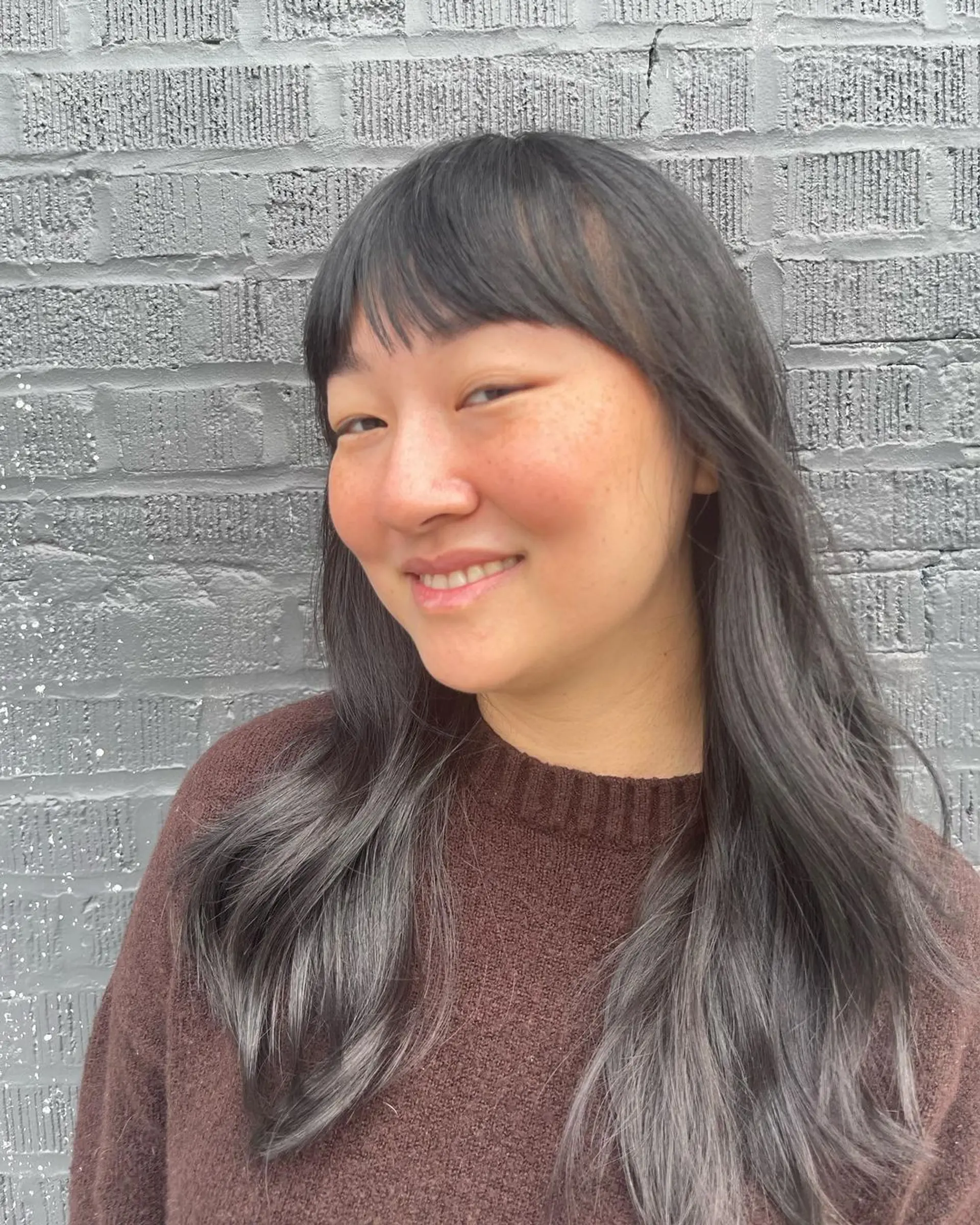 Long, wavy hairstyle with black and gray tones, featuring soft bangs and layered ends for a casual, elegant appearance. 2