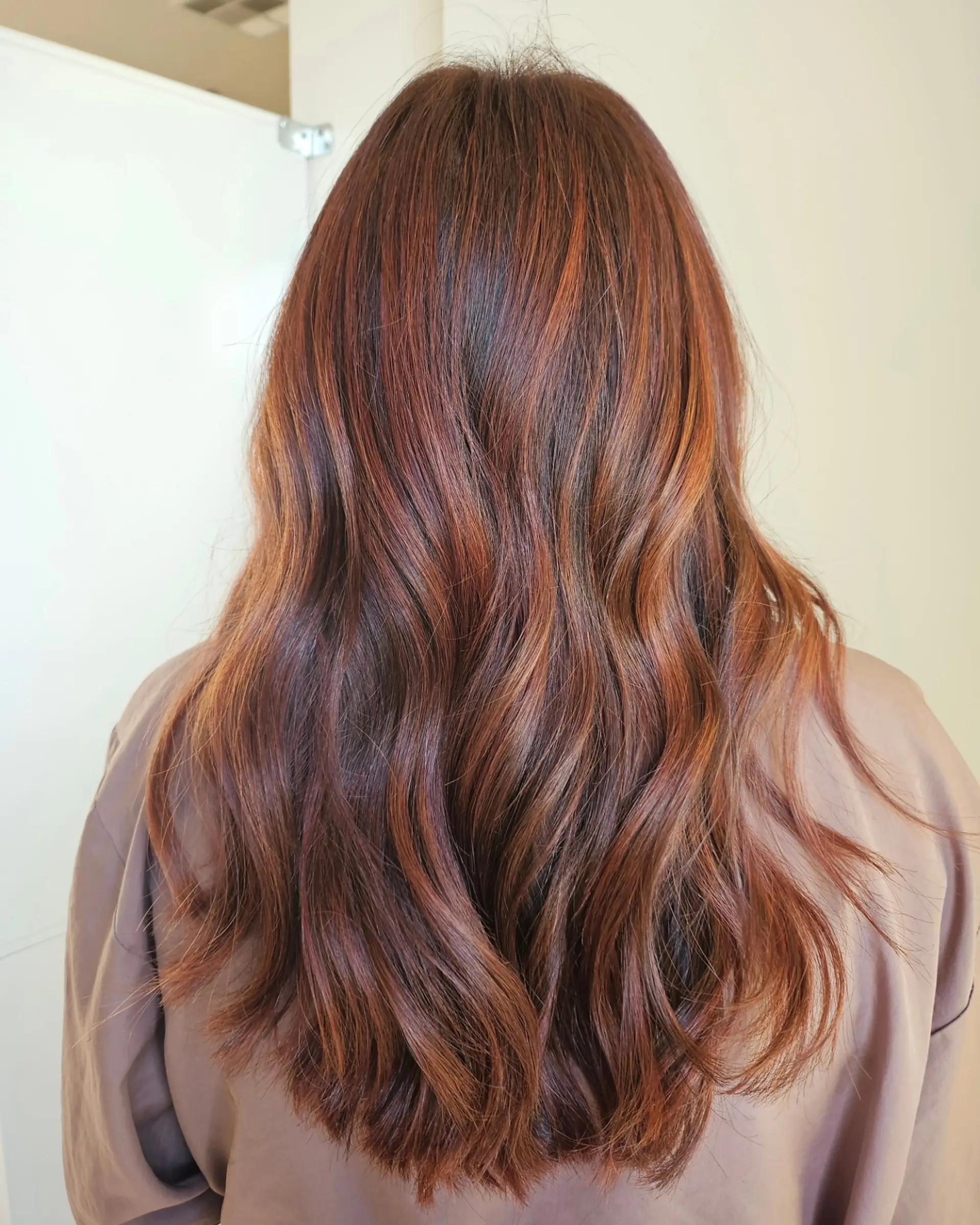 Long cascading waves featuring warm auburn and copper balayage highlights blended over a deep brown base. 1