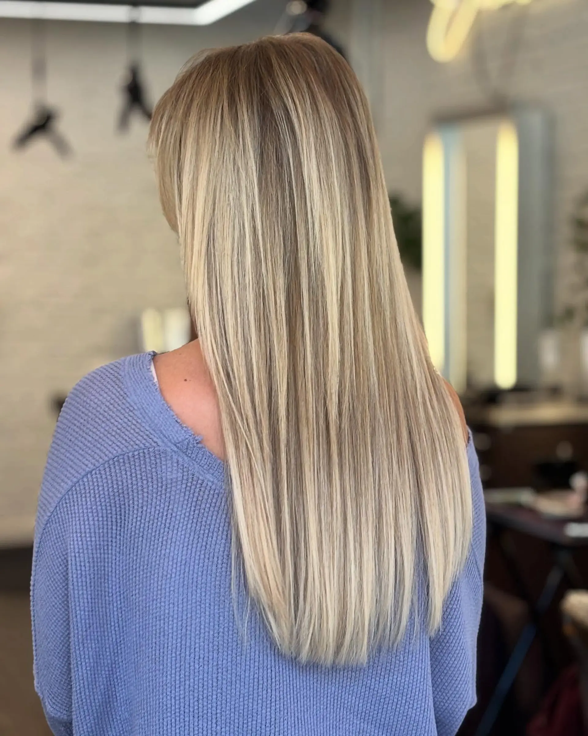 A long, straight hairstyle with a seamless blend of light blonde tones using the balayage technique, creating a buttery blonde effect with face framing layers and a subtle shadow root. 1