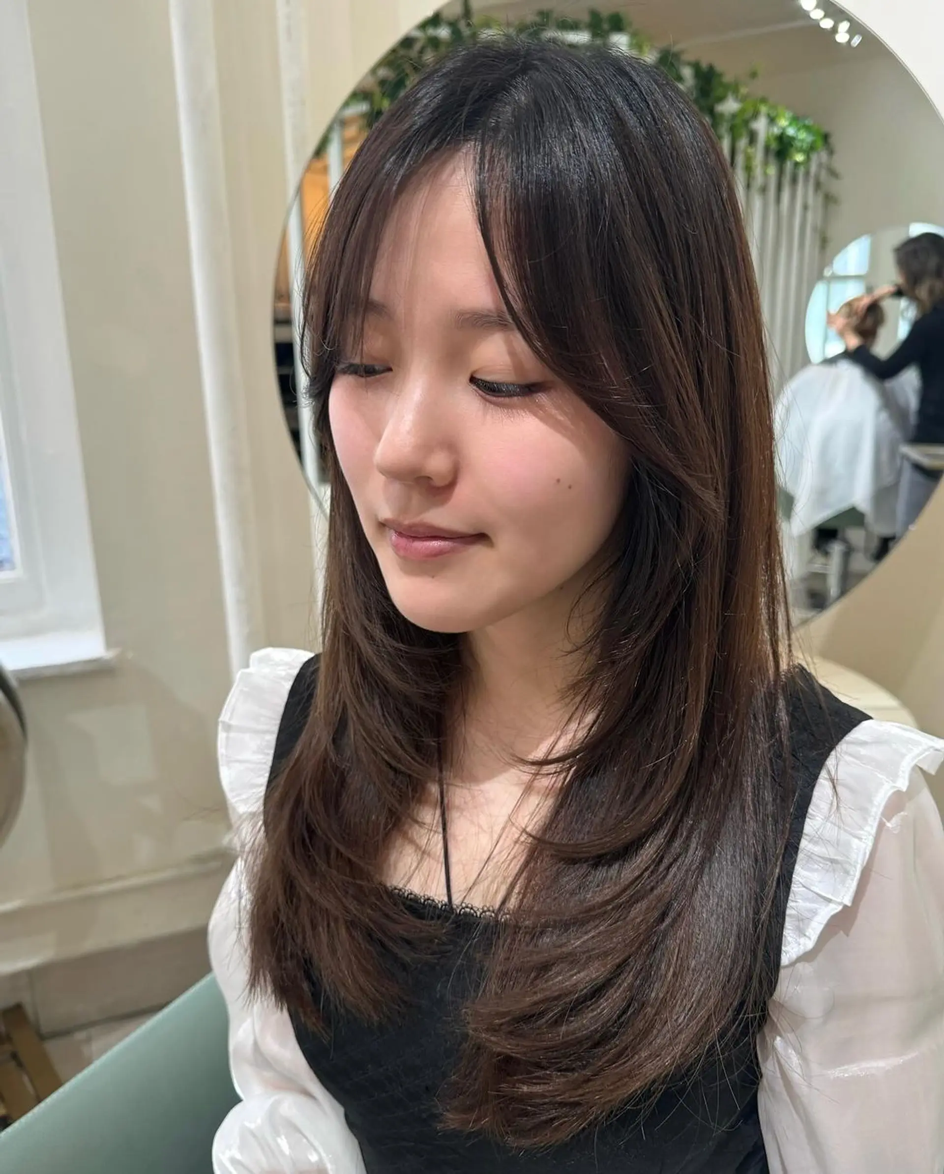 Long, dark brown, straight hair with face-framing layers and subtle side bangs. The natural shine and gentle flow of the hair create a chic and elegant look. 1