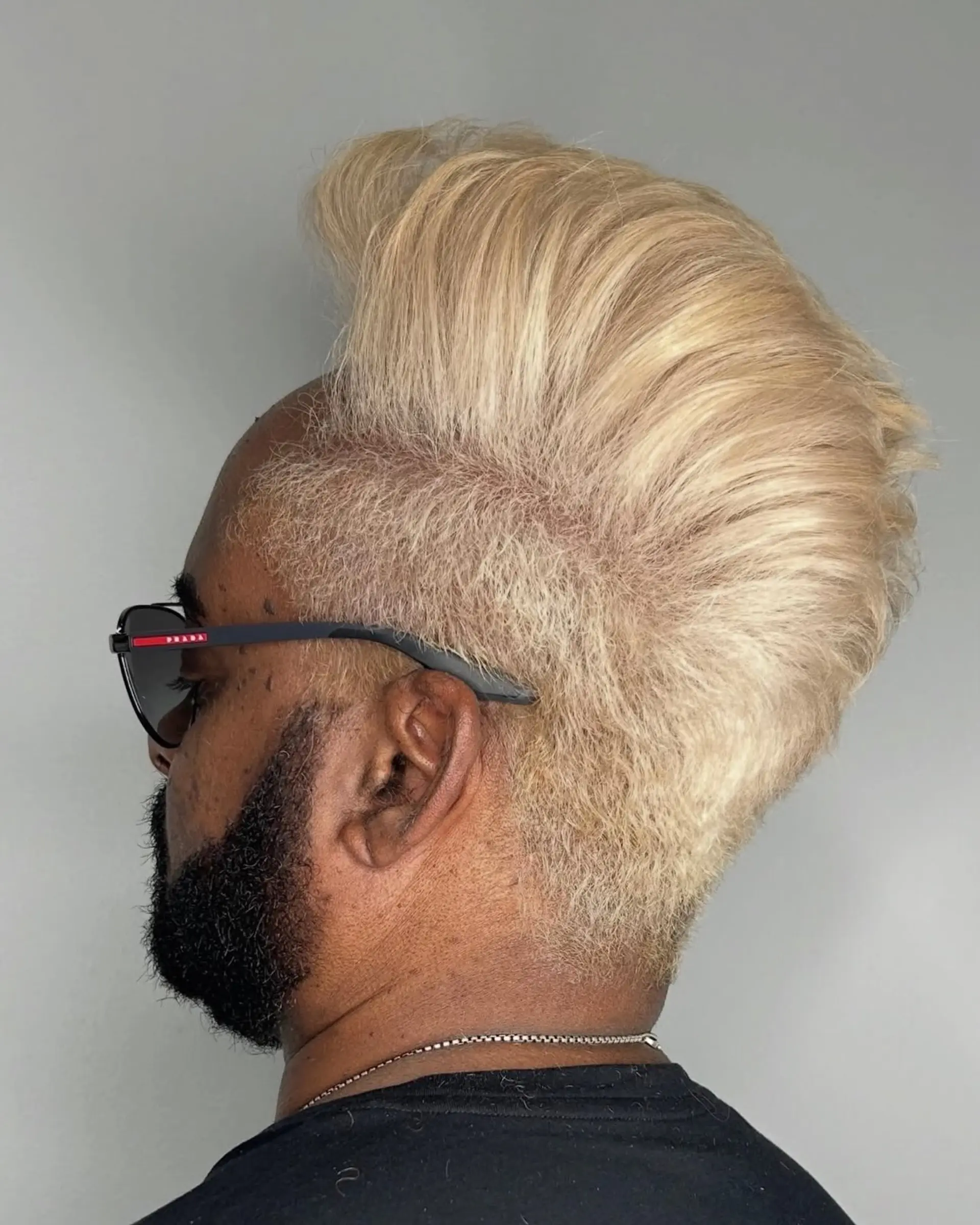 A striking platinum blonde high-volume pompadour styled upwards and backwards, contrasted with clipped faded sides and a natural dark beard. 1