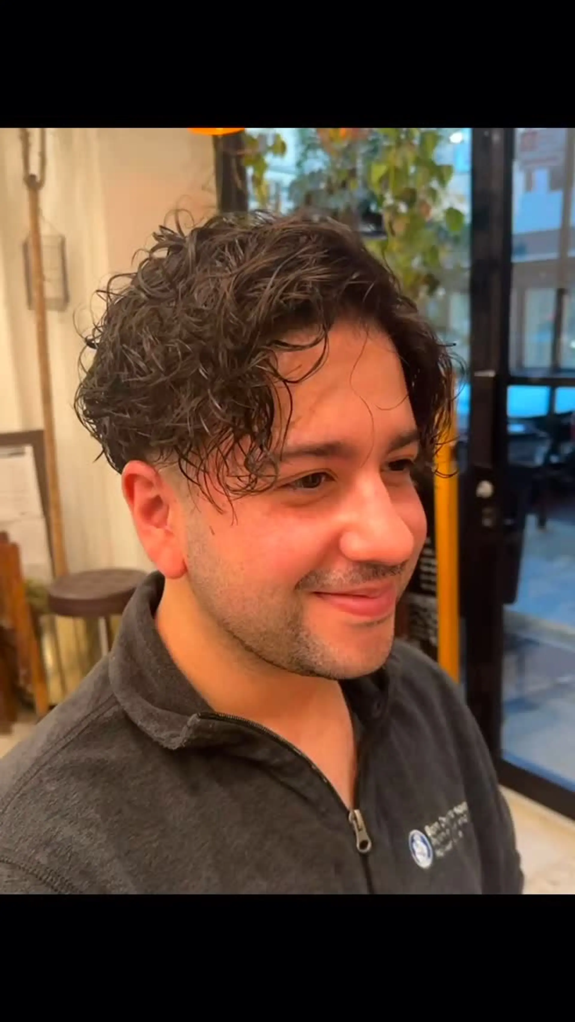 A textured short men's cut with defined curls on top falling into a soft, tousled front fringe and neatly tapered sides. 1