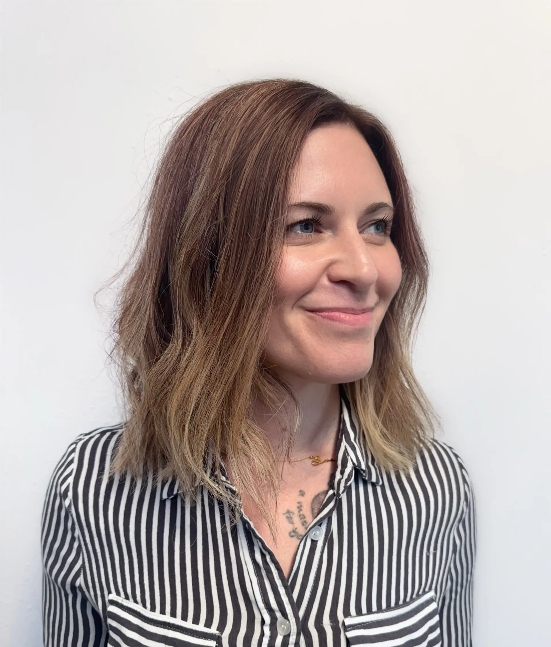 A collarbone-length textured wavy lob featuring a transitional bronde color with subtle warm brunette roots and lighter ends. 1