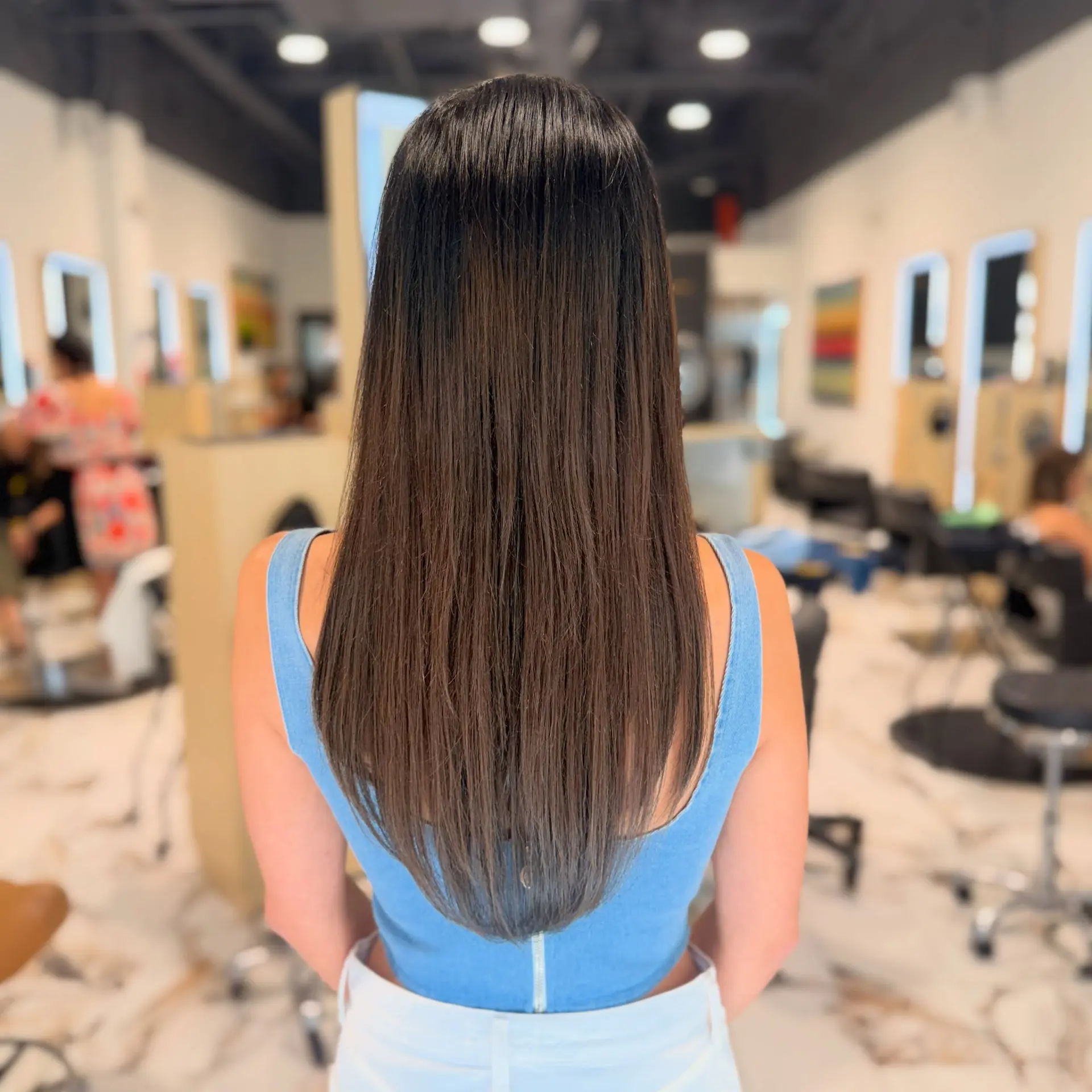 Long, sleek dark brunette hair featuring seamless extensions cut into a soft V-shape taper. 1