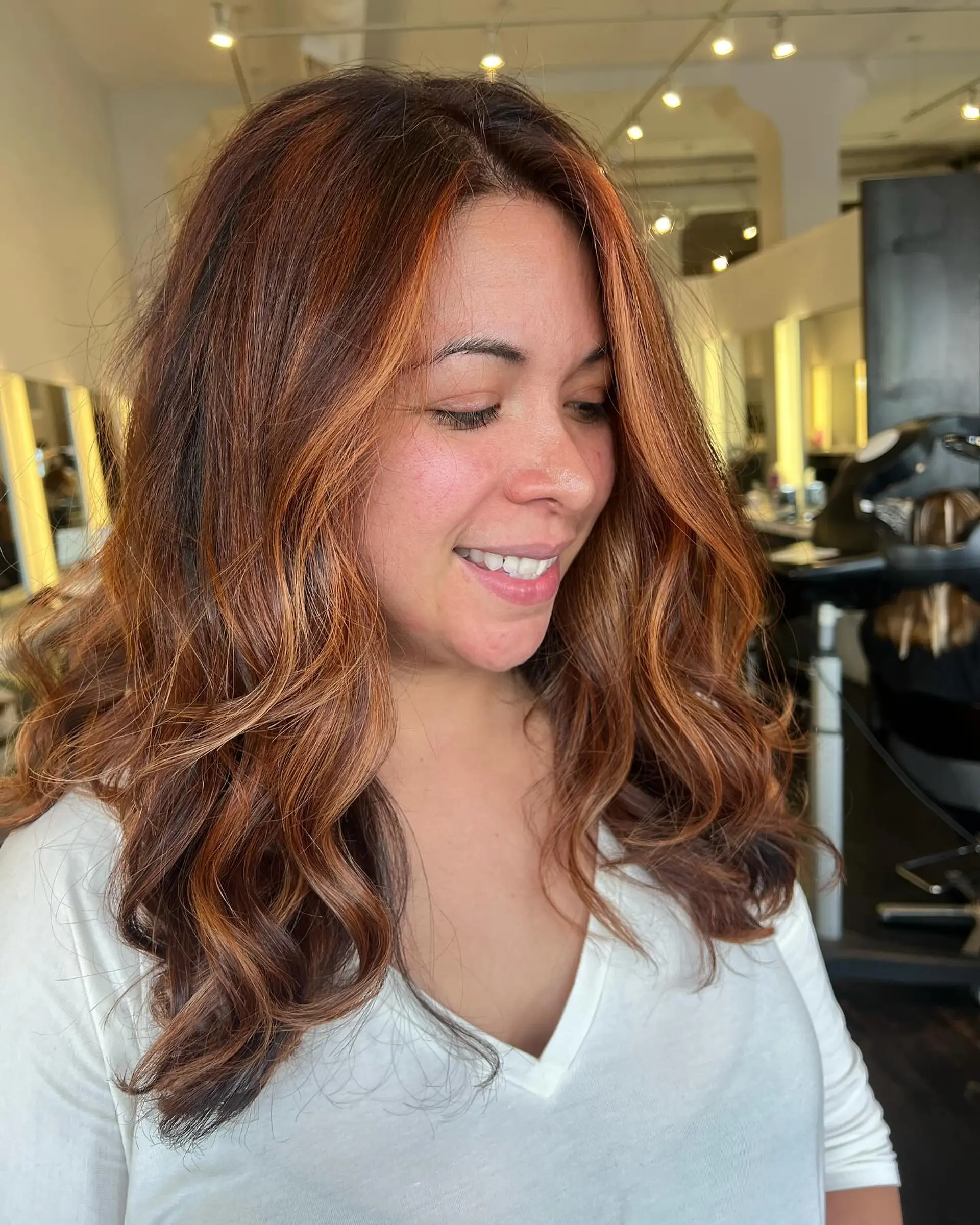 Rich copper balayage highlights over a warm brunette base, styled in loose, voluminous waves with bright face-framing accents. 1