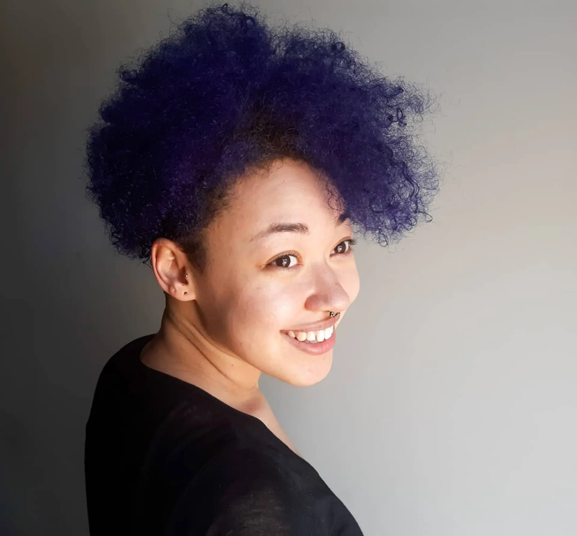 A bold, curly hairstyle featuring an undercut and a vibrant indigo color. 2